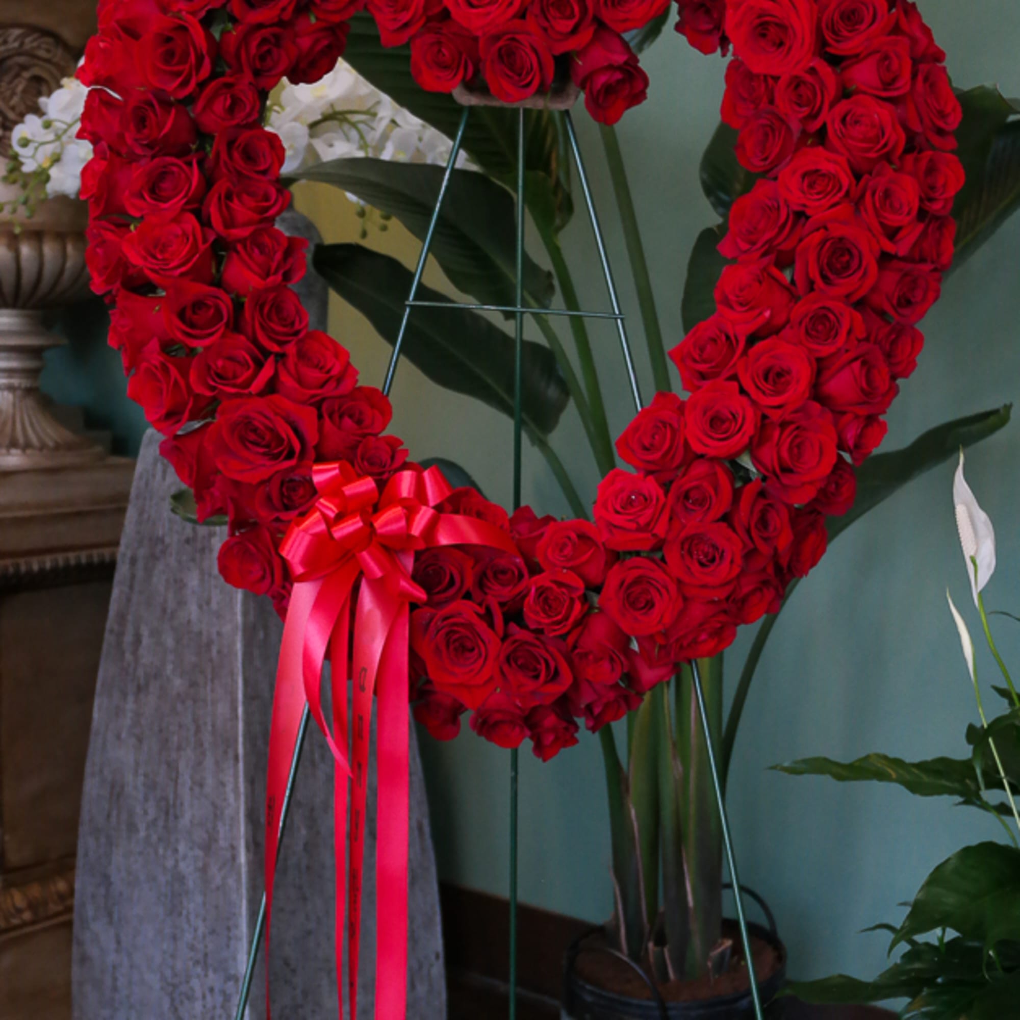 Heart-shaped red rose standing arrangement with a pink ribbon