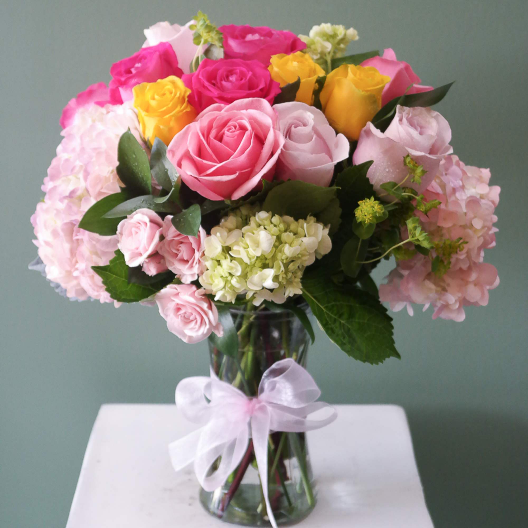 Pink, yellow, and white roses in a glass vase with a ribbon