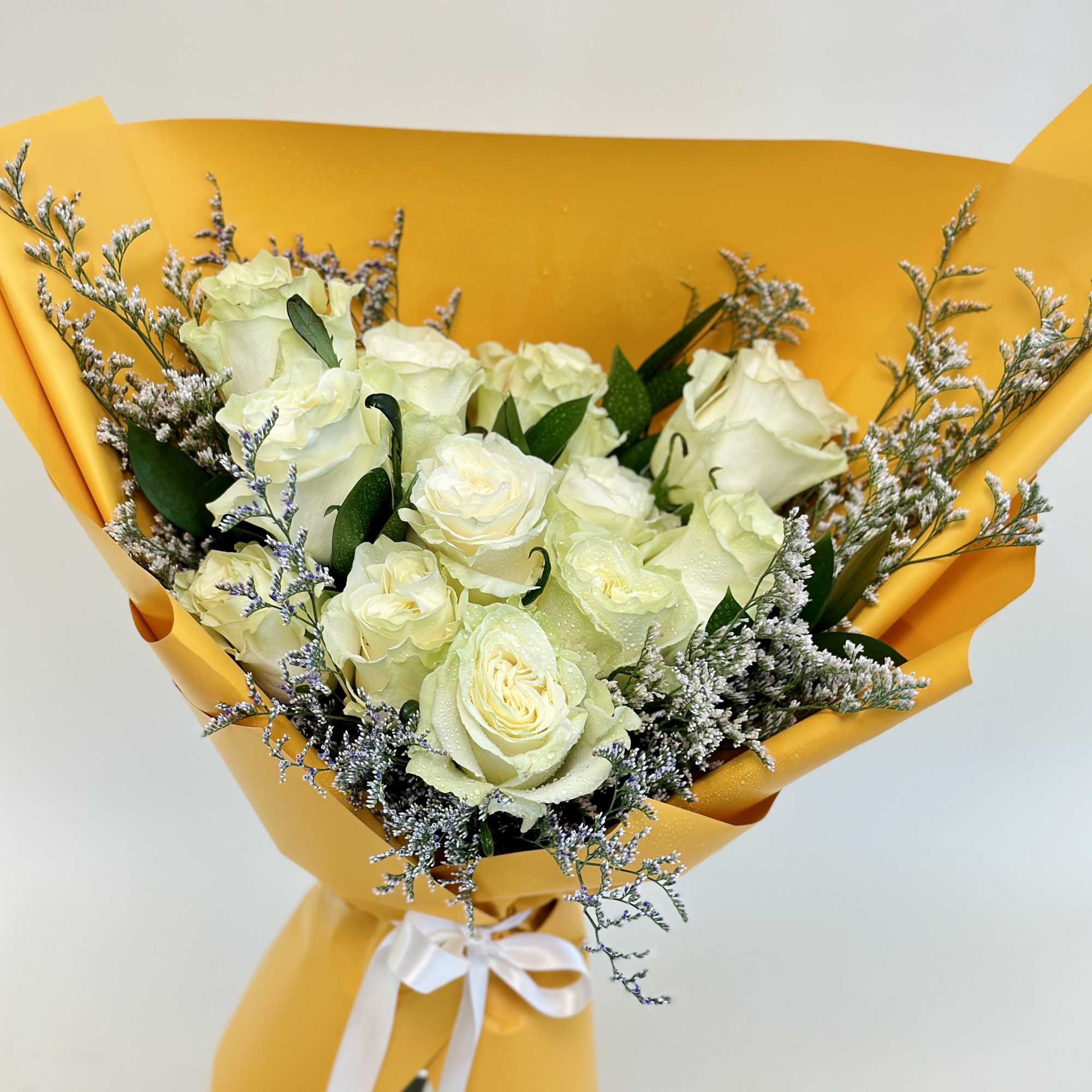 Bouquet of white roses wrapped in bright yellow paper