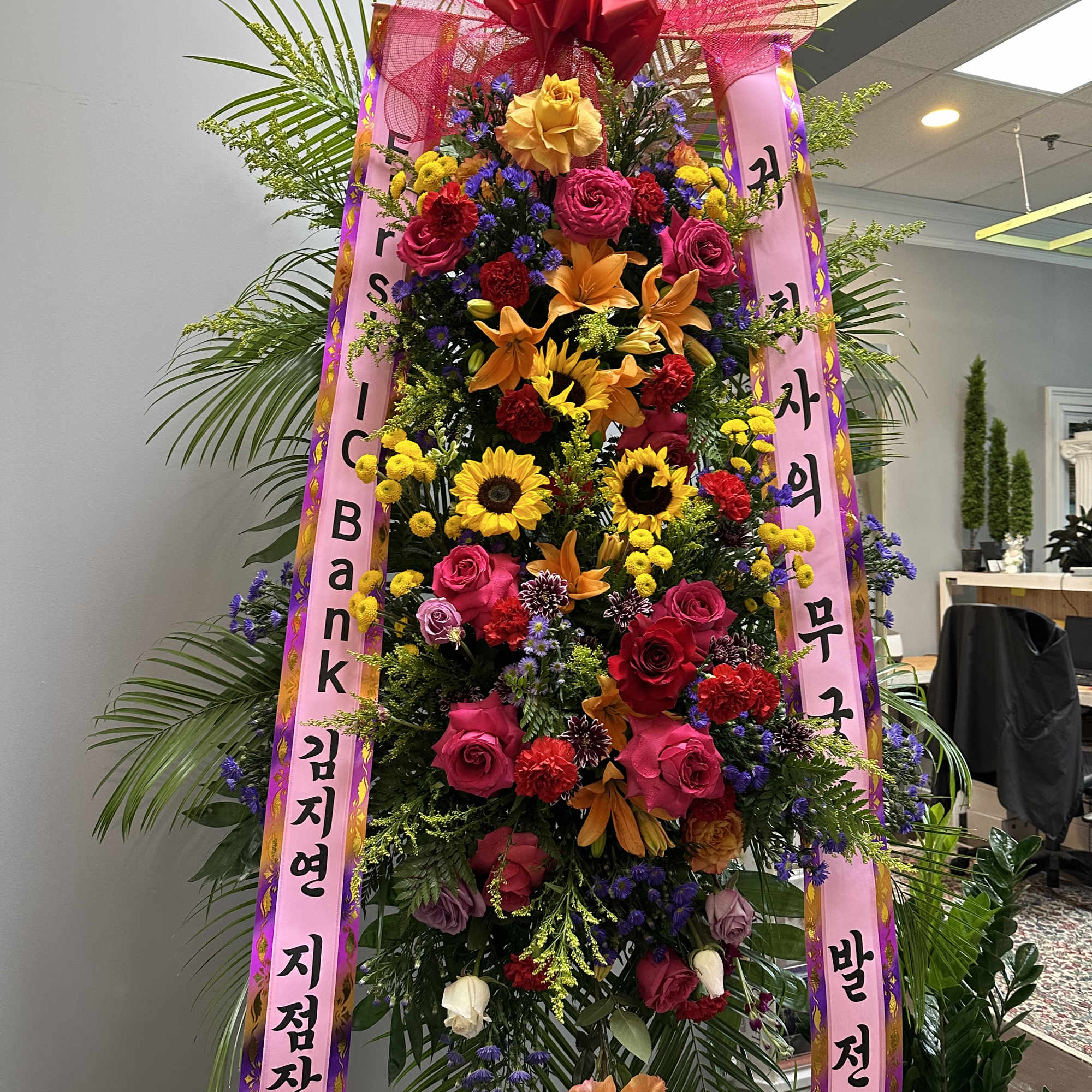 Tall standing floral wreath with pink ribbons and mixed blooms