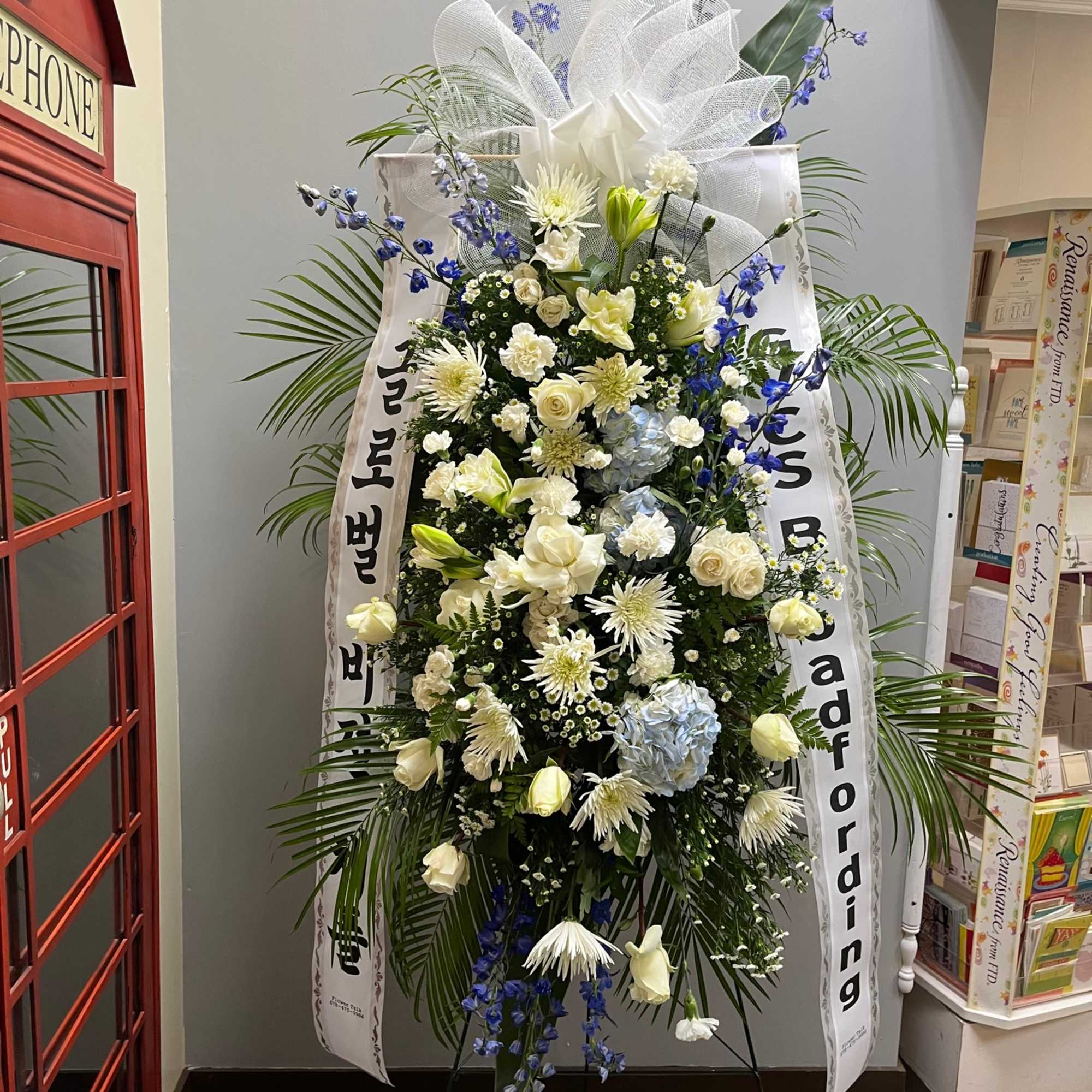 Tall white and blue funeral spray with ribbon on an easel