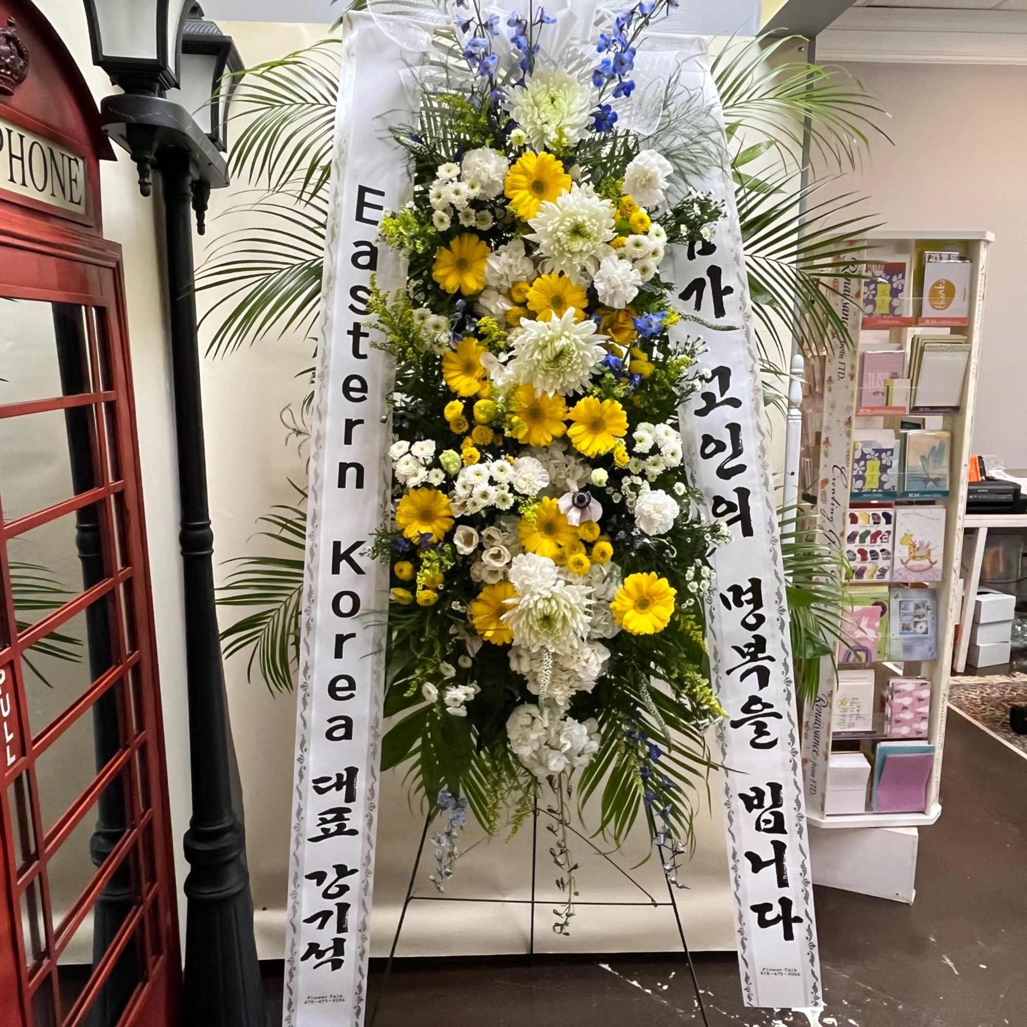 Tall standing floral spray with yellow and white blooms on a display easel