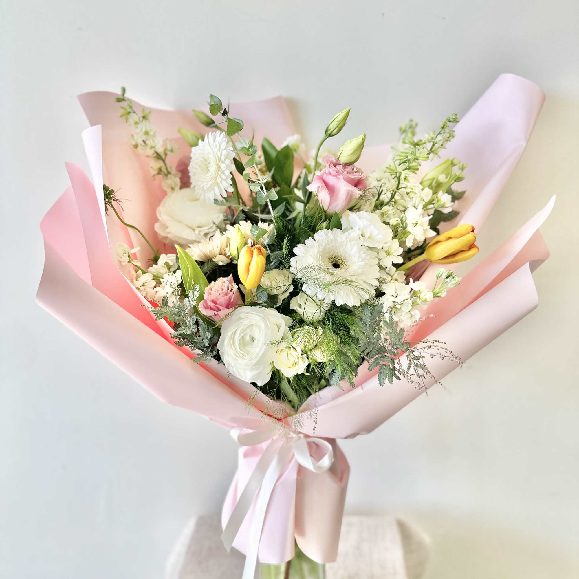 Pastel bouquet of white, pink, and yellow flowers wrapped in pink paper