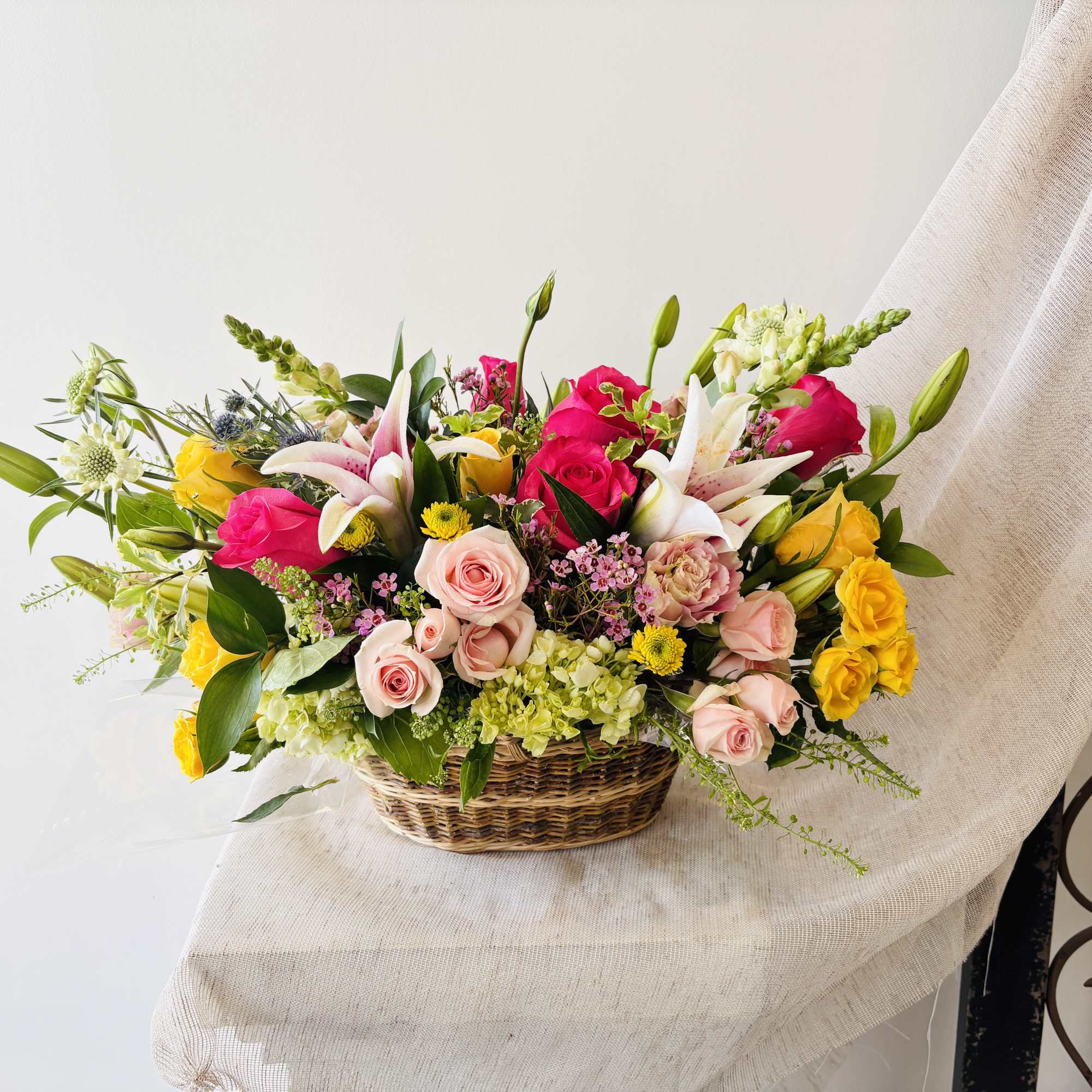 Mixed bouquet of pink, yellow, and white flowers in a wicker basket