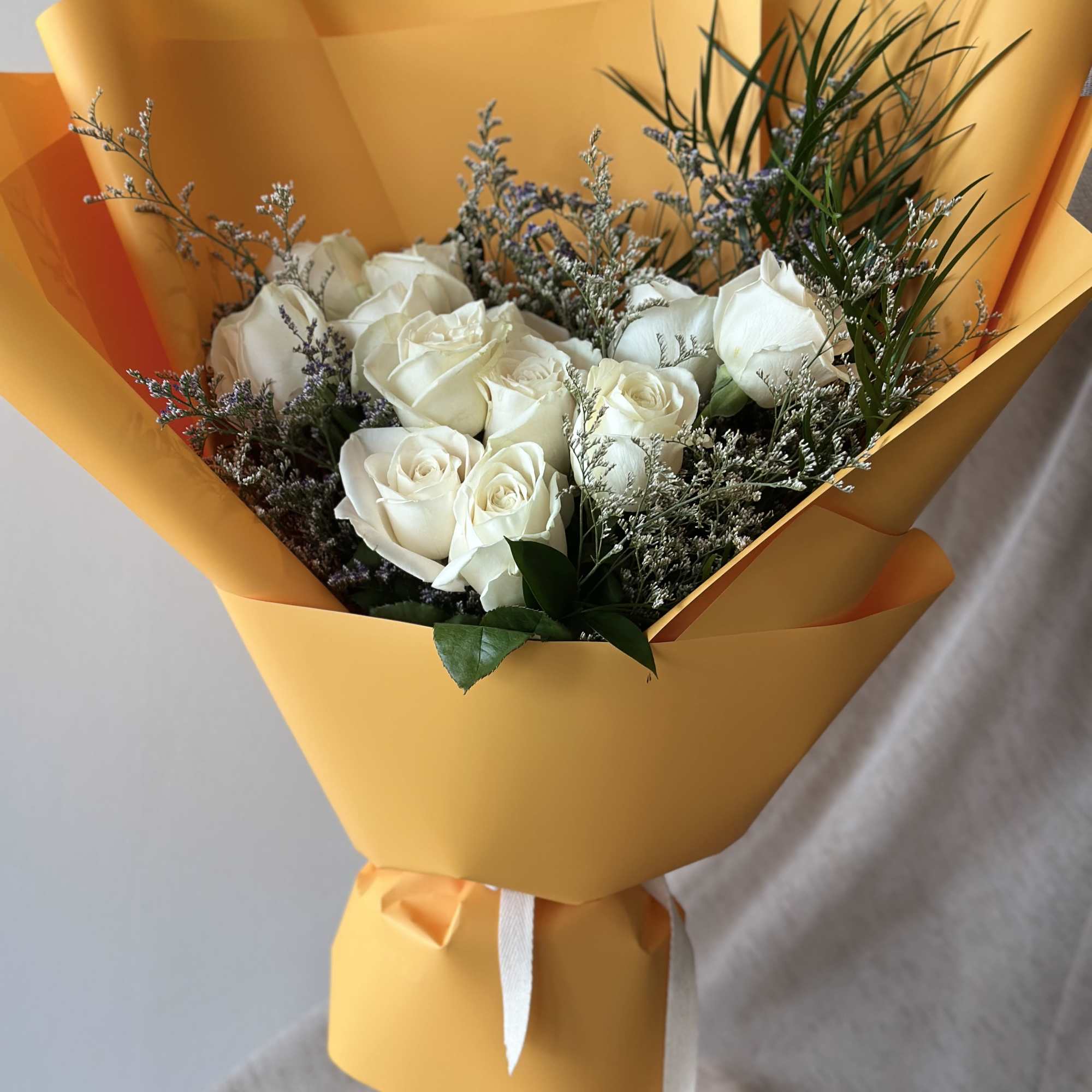 White roses in orange wrapping with a clear glass vase