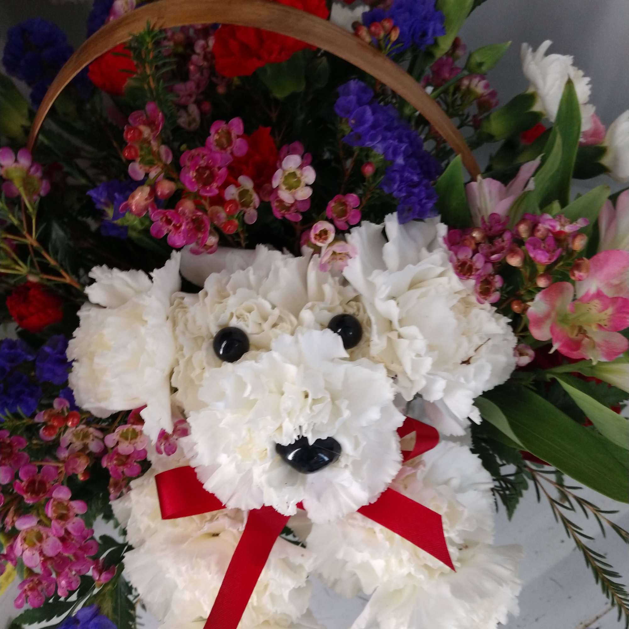 White flower teddy bear basket with a red ribbon and colorful blooms