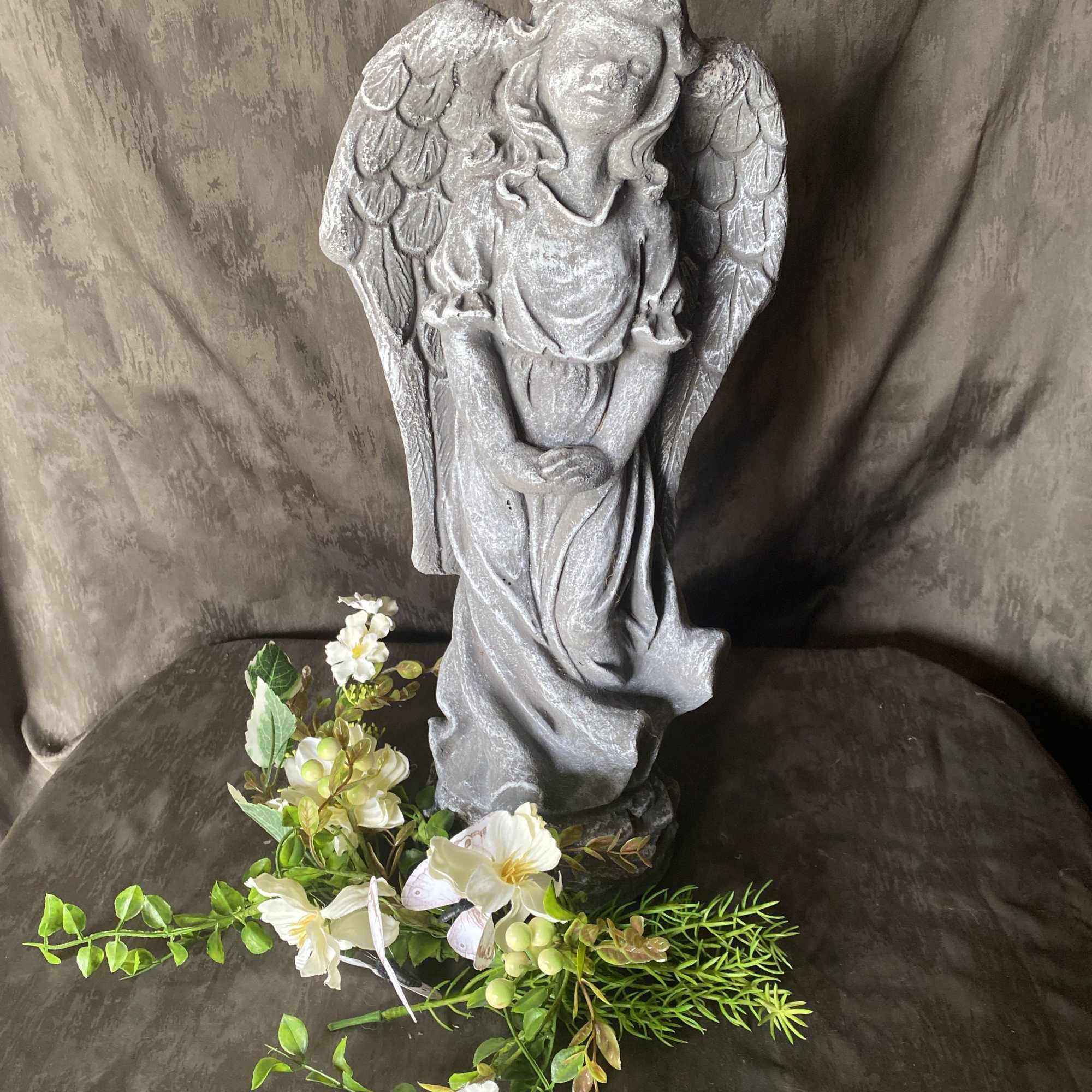 Gray angel statue with a small white floral spray at the base