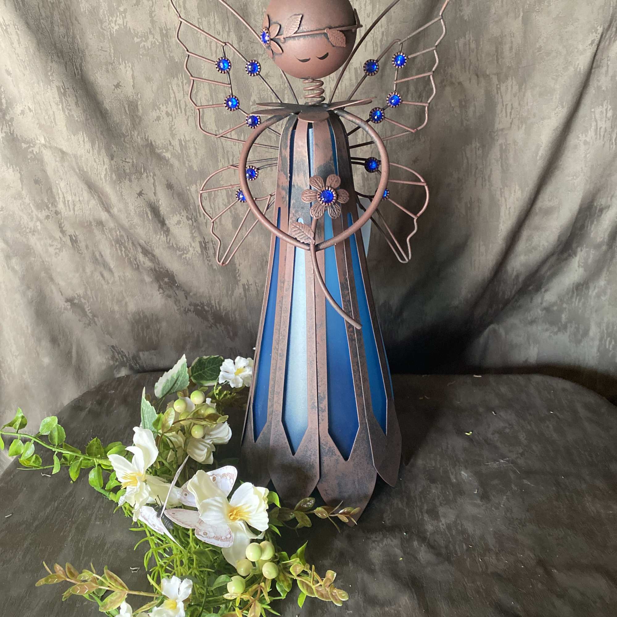 Metal angel figurine with blue accents and white flowers at the base