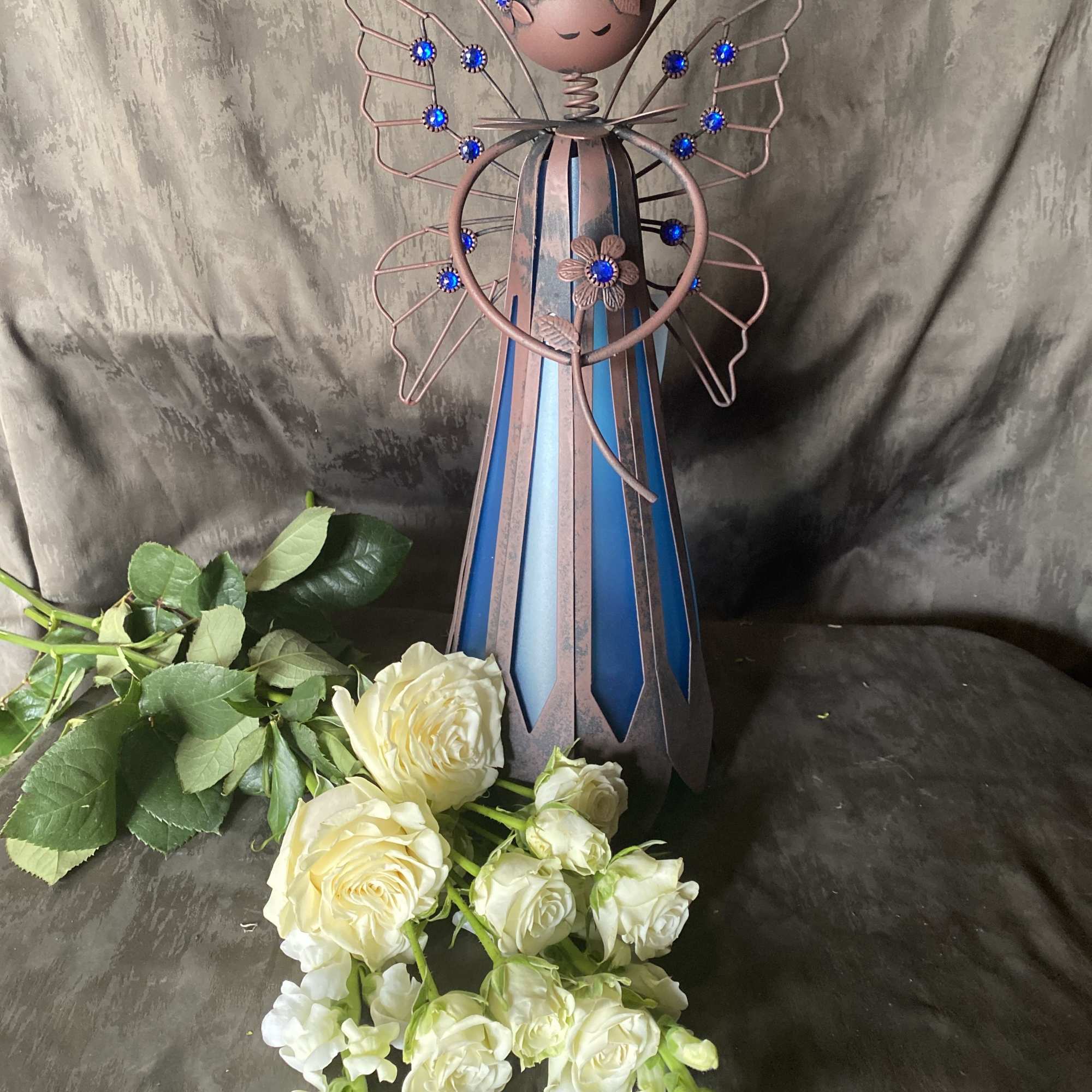 Metal angel figurine with white roses and greenery at the base