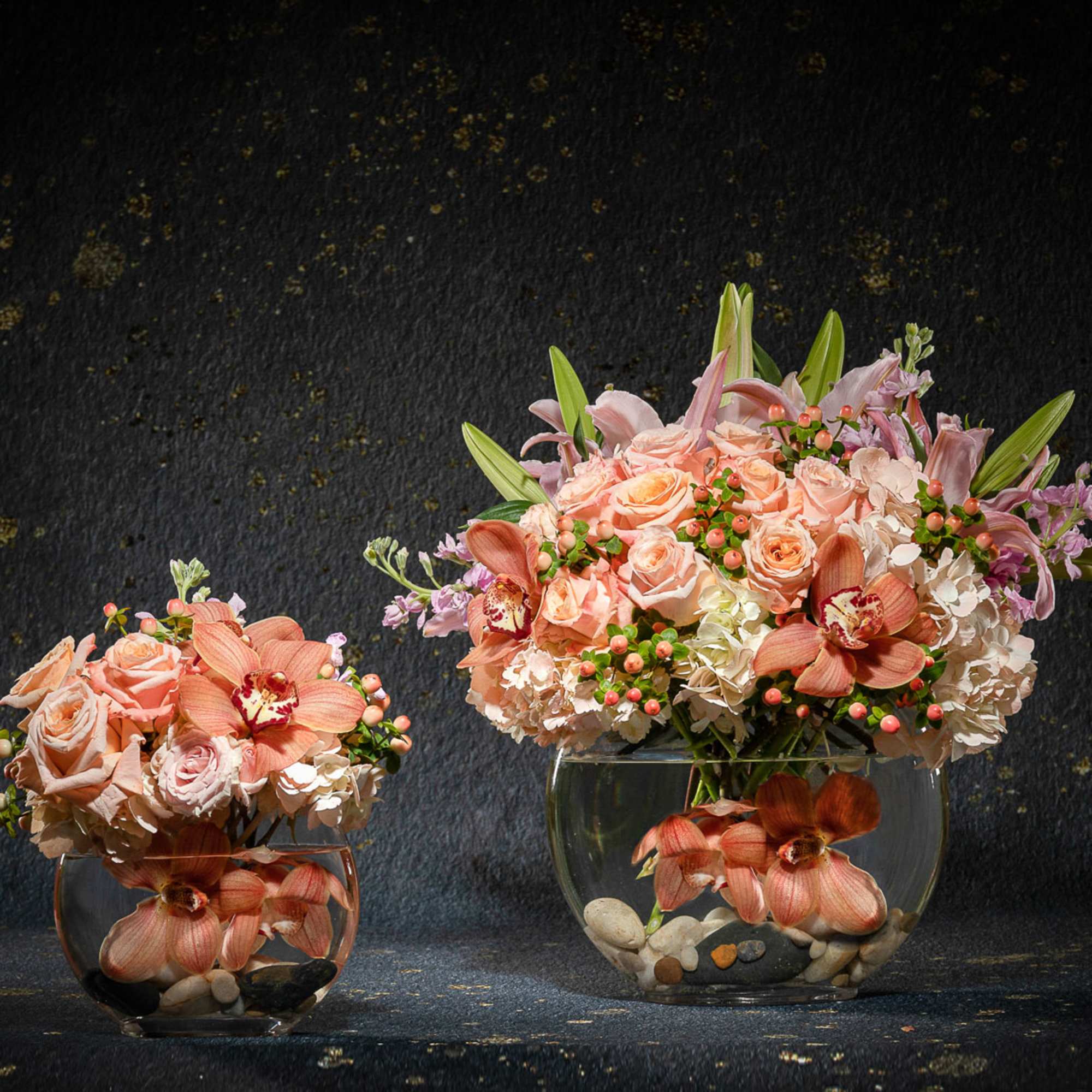 Two peach floral arrangements in clear glass bowls on a dark background.