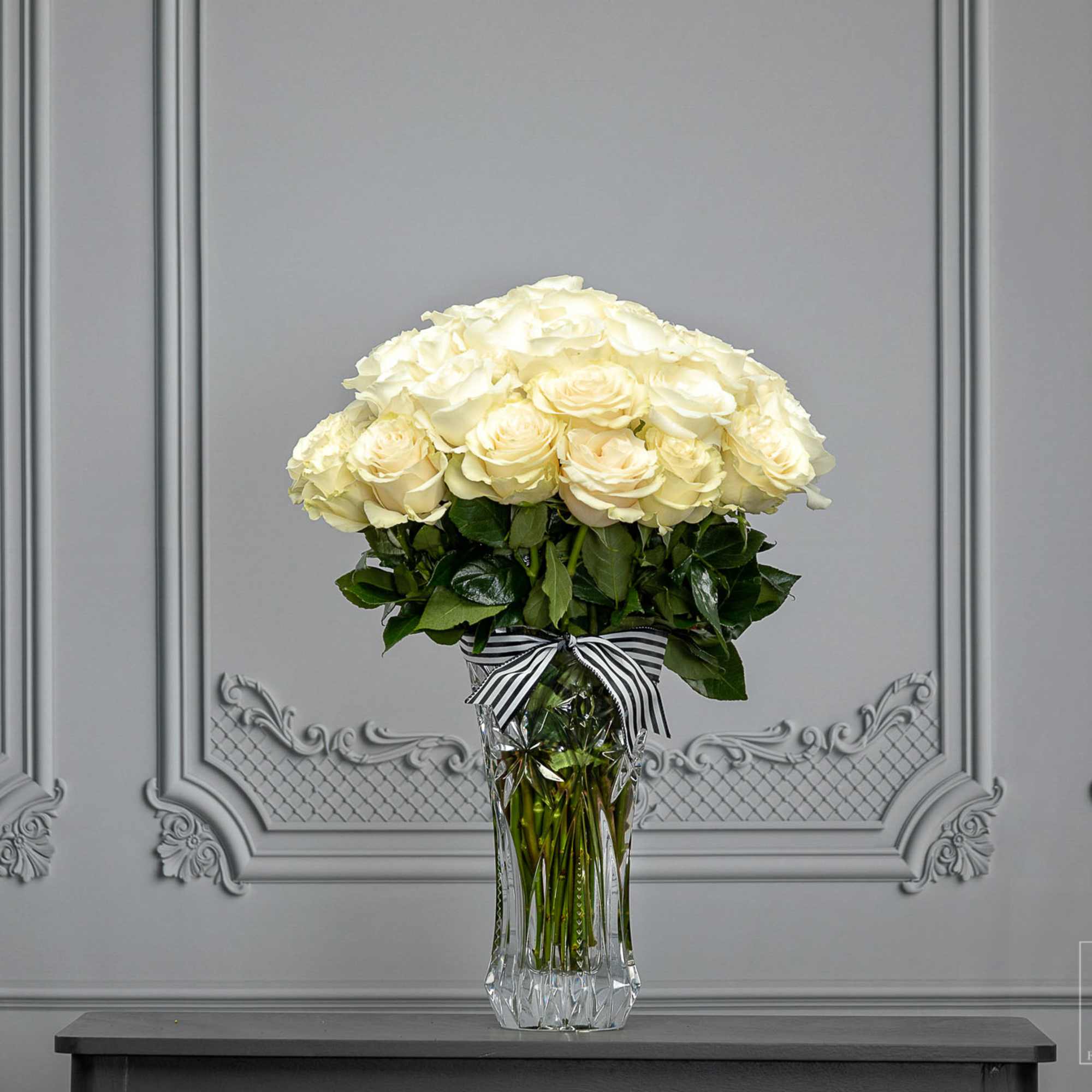 Cream rose bouquet in a clear glass vase with a striped ribbon