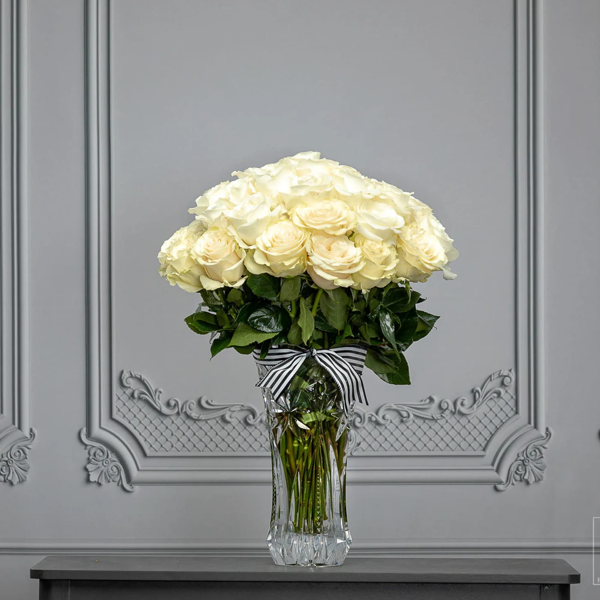 White roses arranged in a clear glass vase with a striped ribbon.