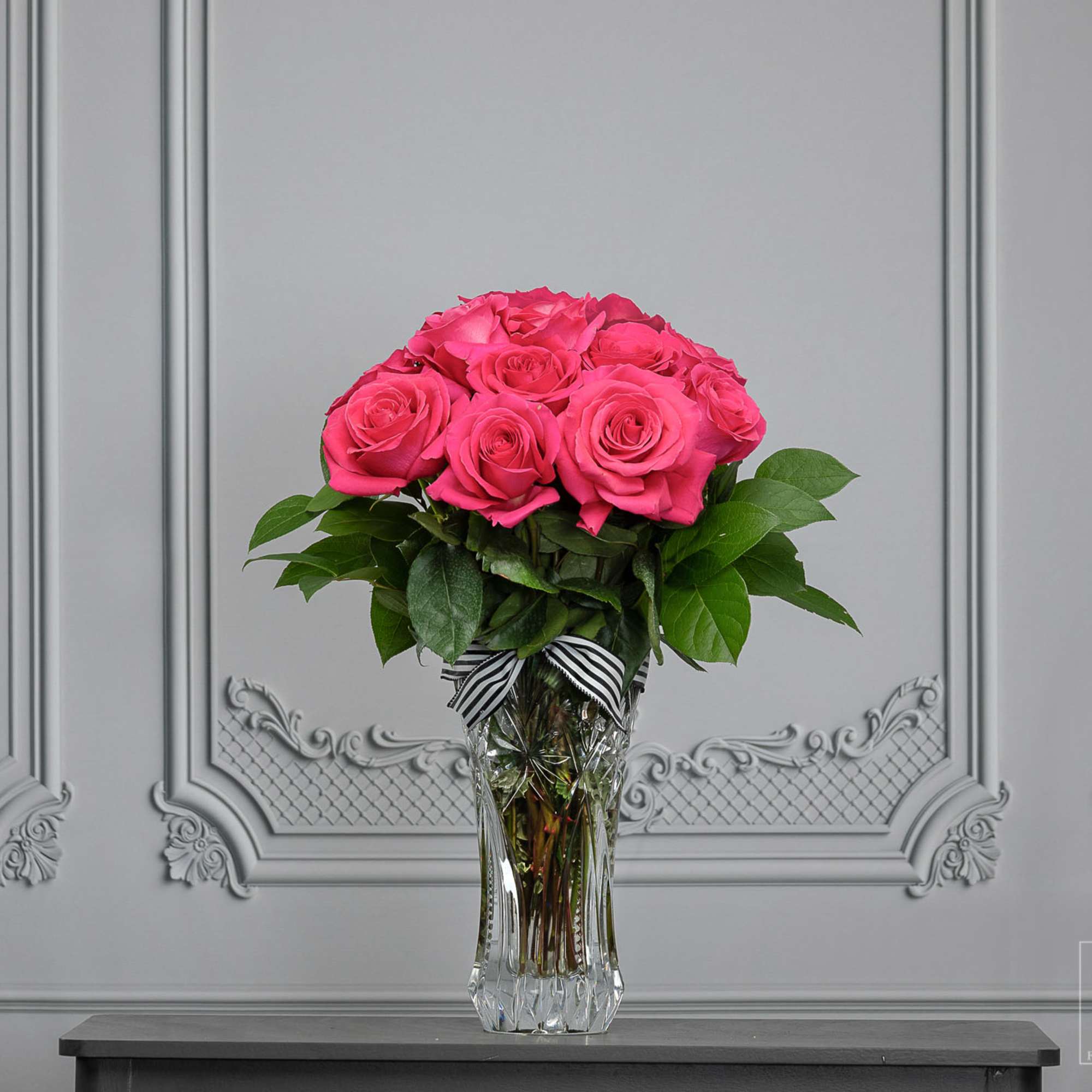 Pink rose bouquet in a clear glass vase with a striped ribbon