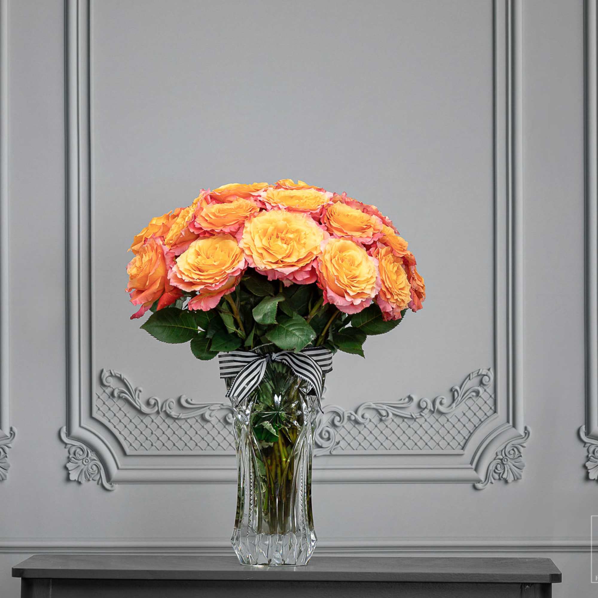 Orange and pink roses in a clear glass vase with a striped ribbon