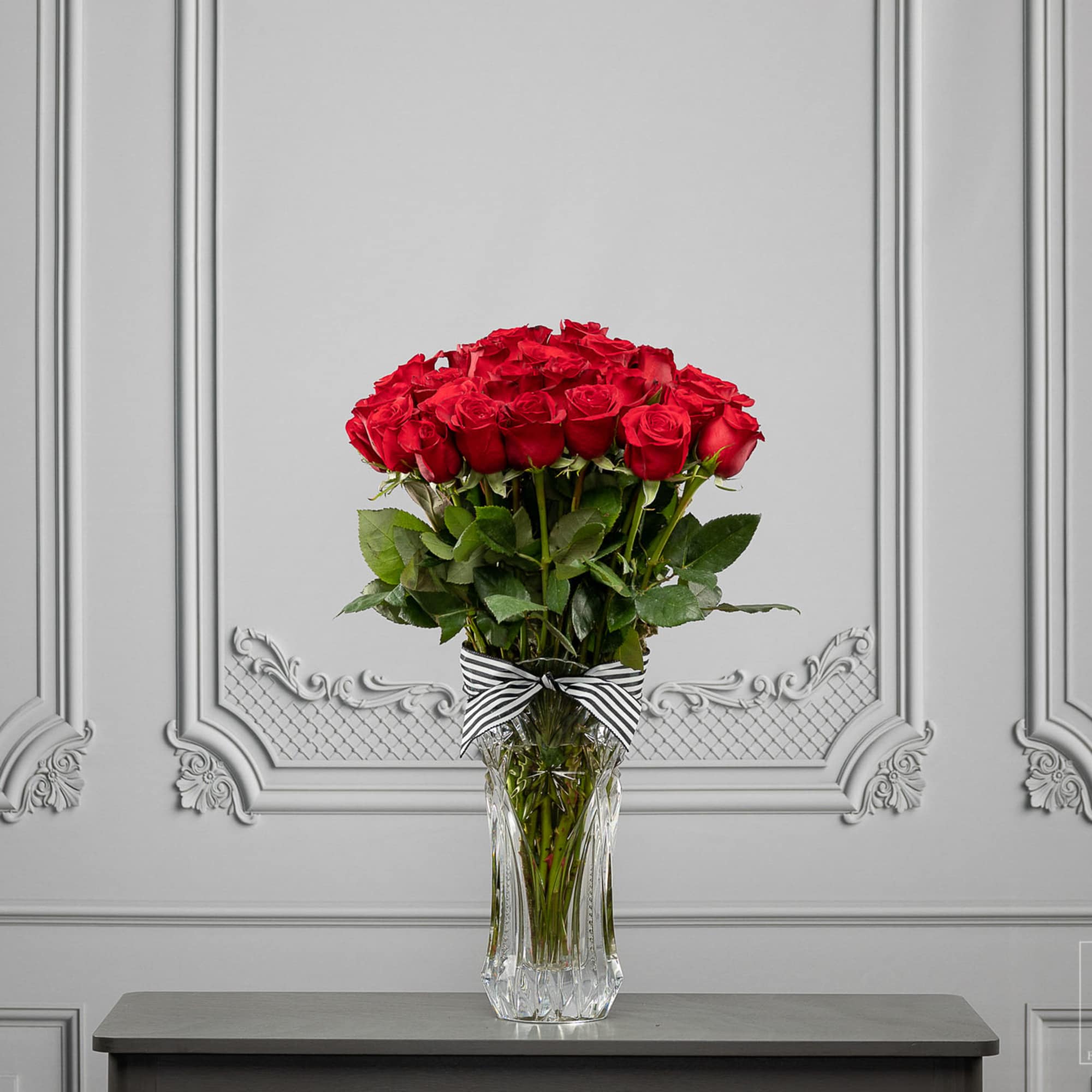 Red roses arranged in a clear glass vase with a striped ribbon