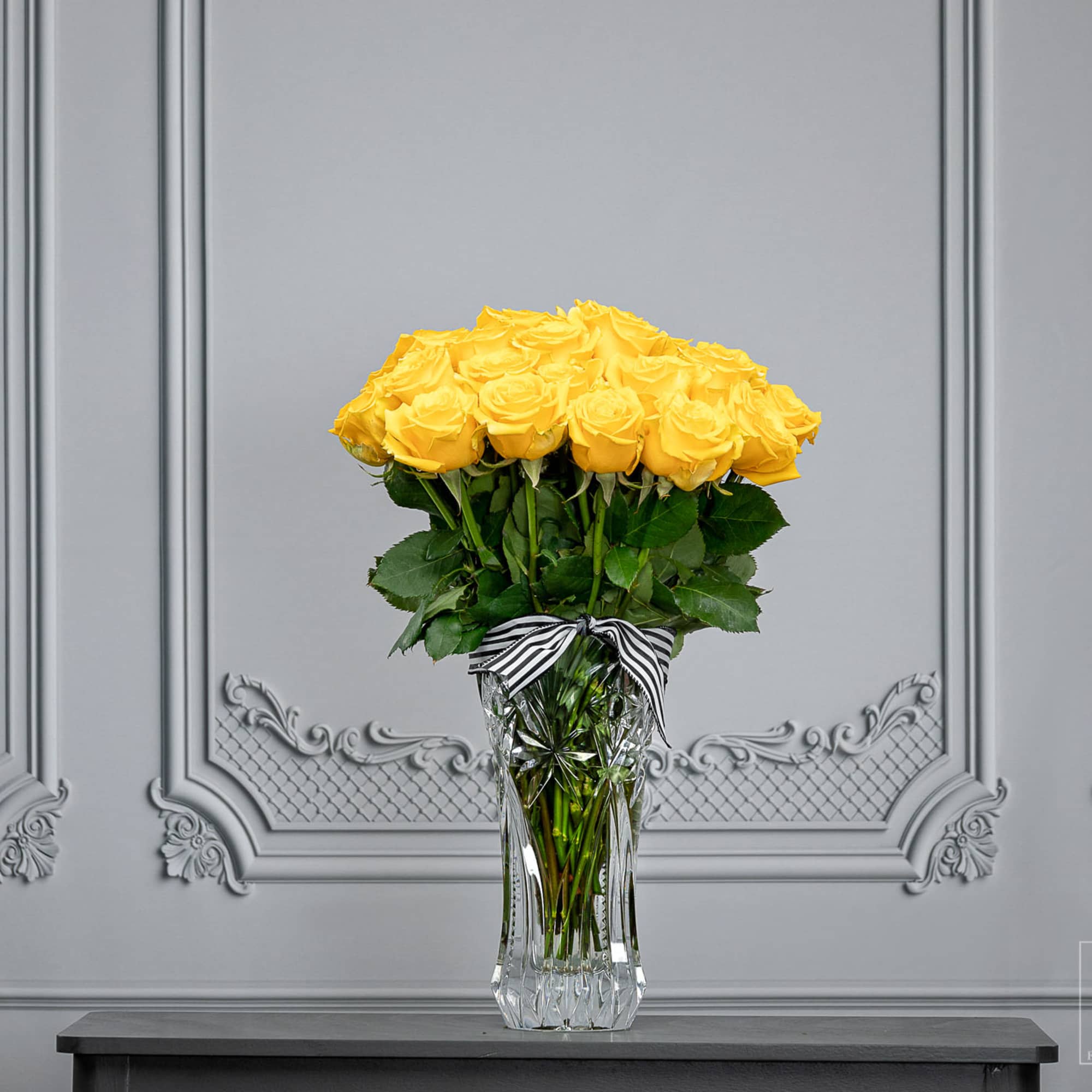 Yellow roses in a clear glass vase with a striped ribbon