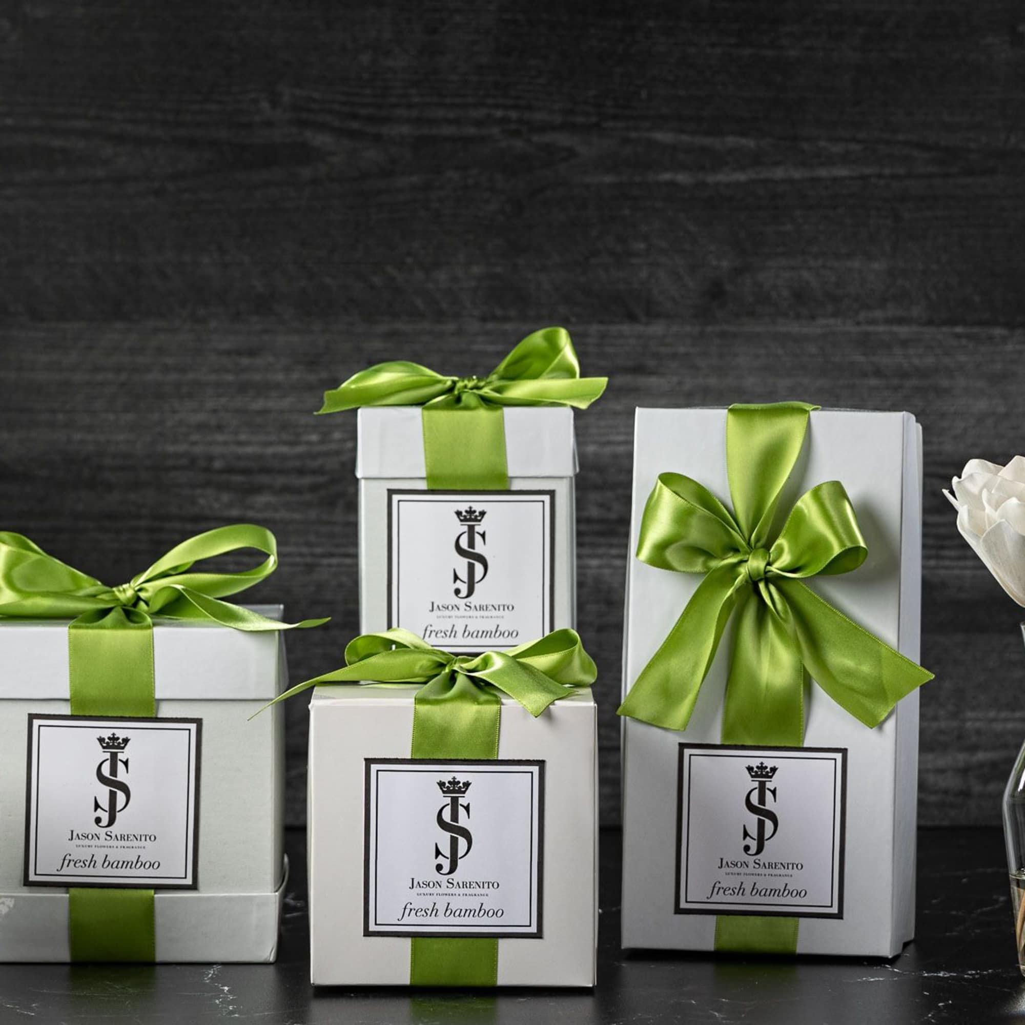 Gift boxes with green ribbons, a candle, and white flowers in a vase