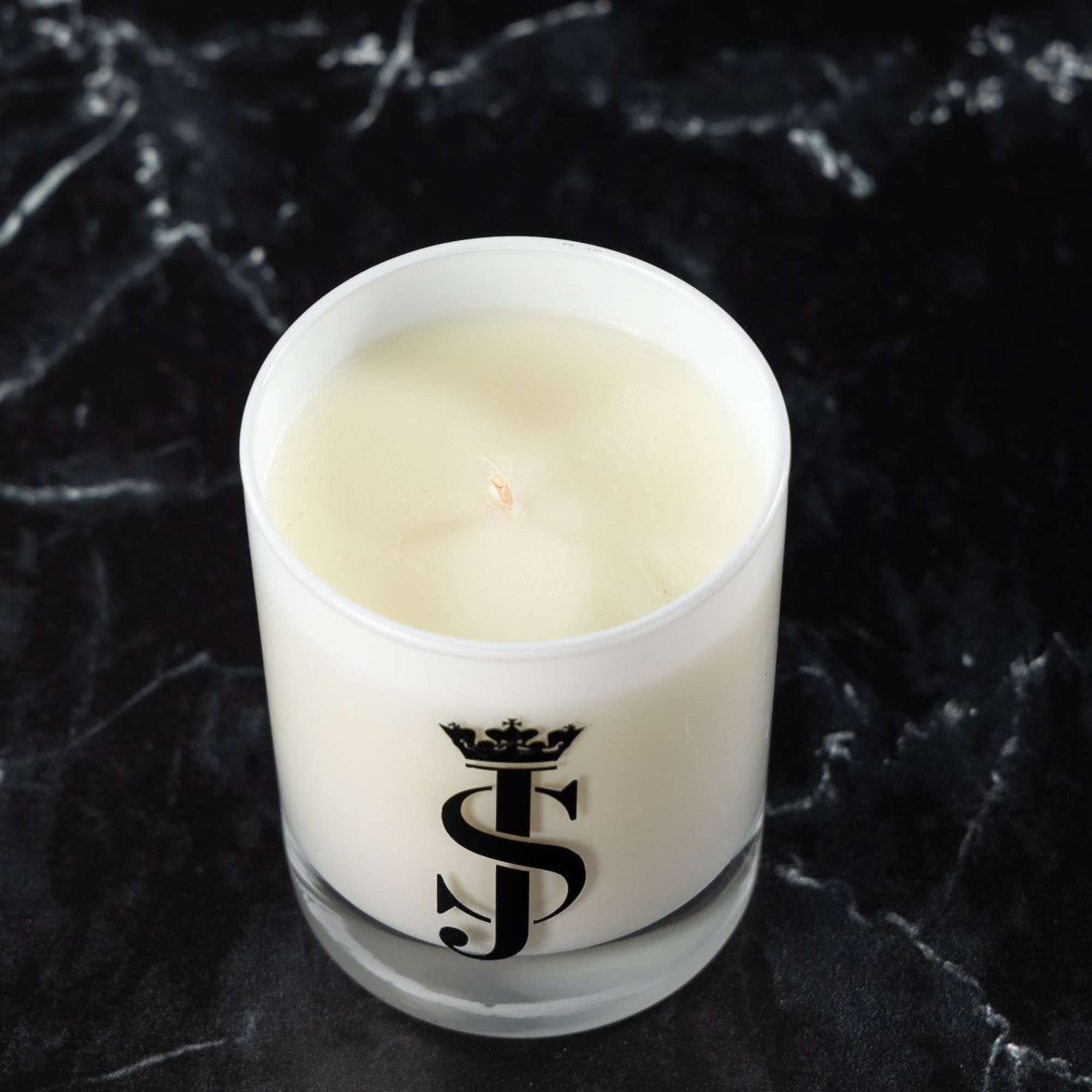 White candle in a glass container with a black monogram logo