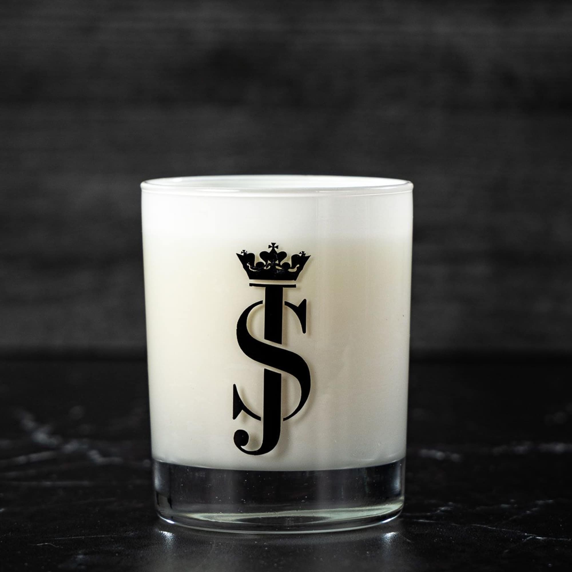 White candle in a clear glass tumbler with a black monogram logo