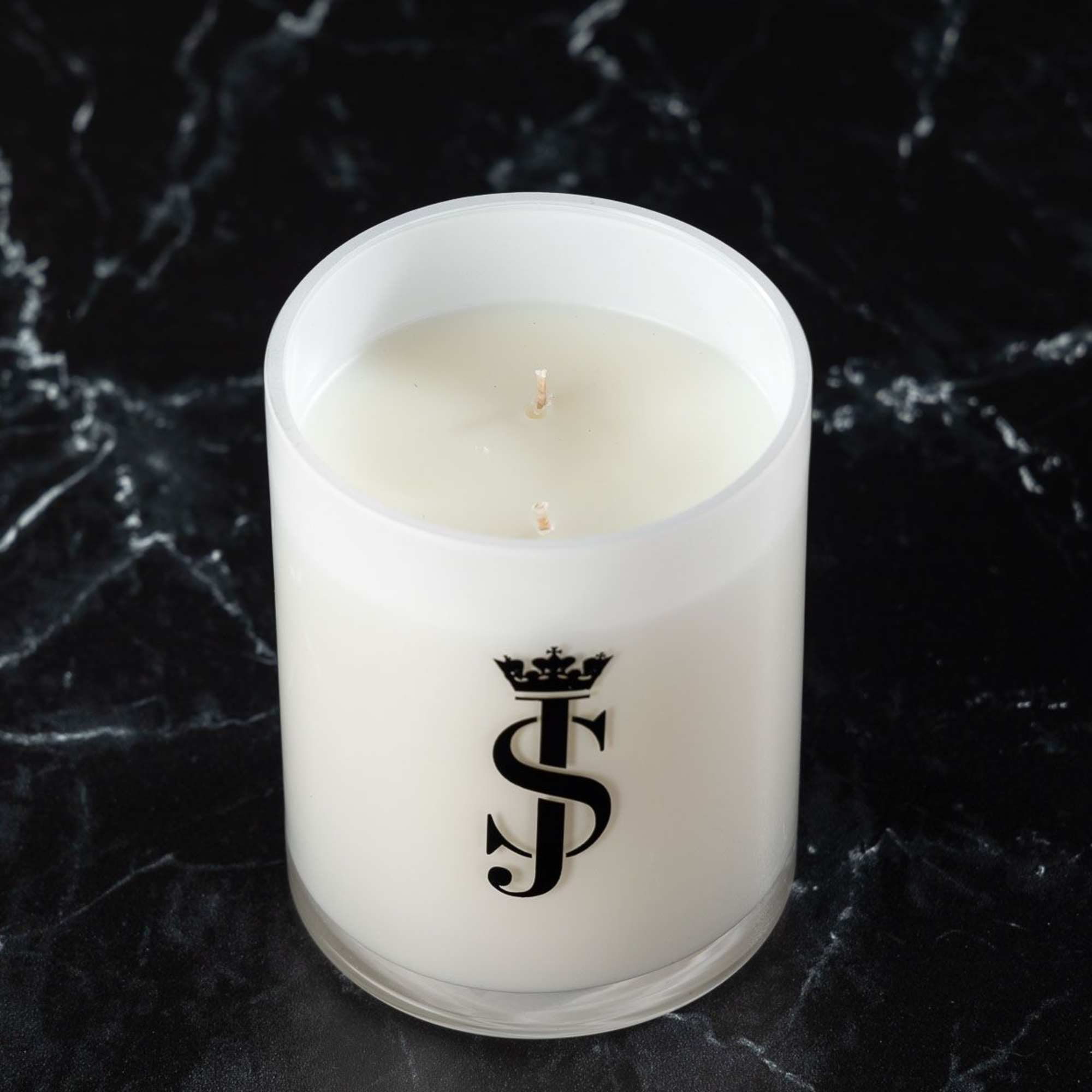 White candle in a frosted glass container with a black monogram logo