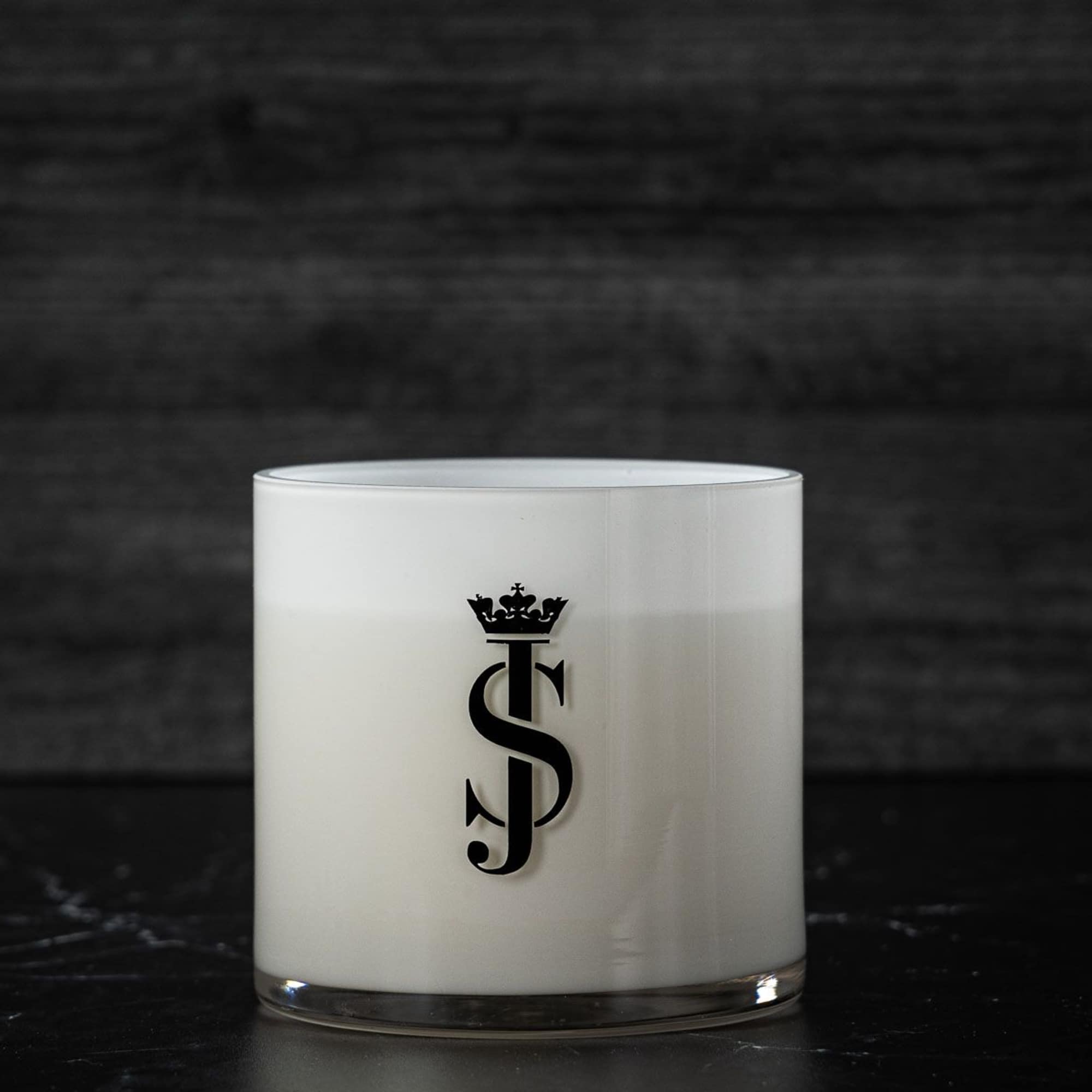 White glass candle with a black monogram logo