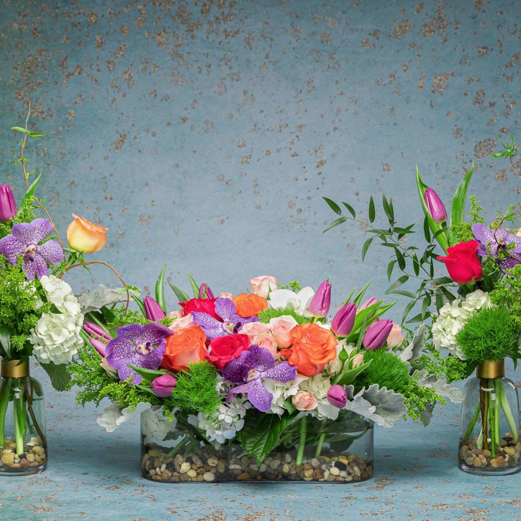 Three colorful floral arrangements in glass vases and a low rectangular container