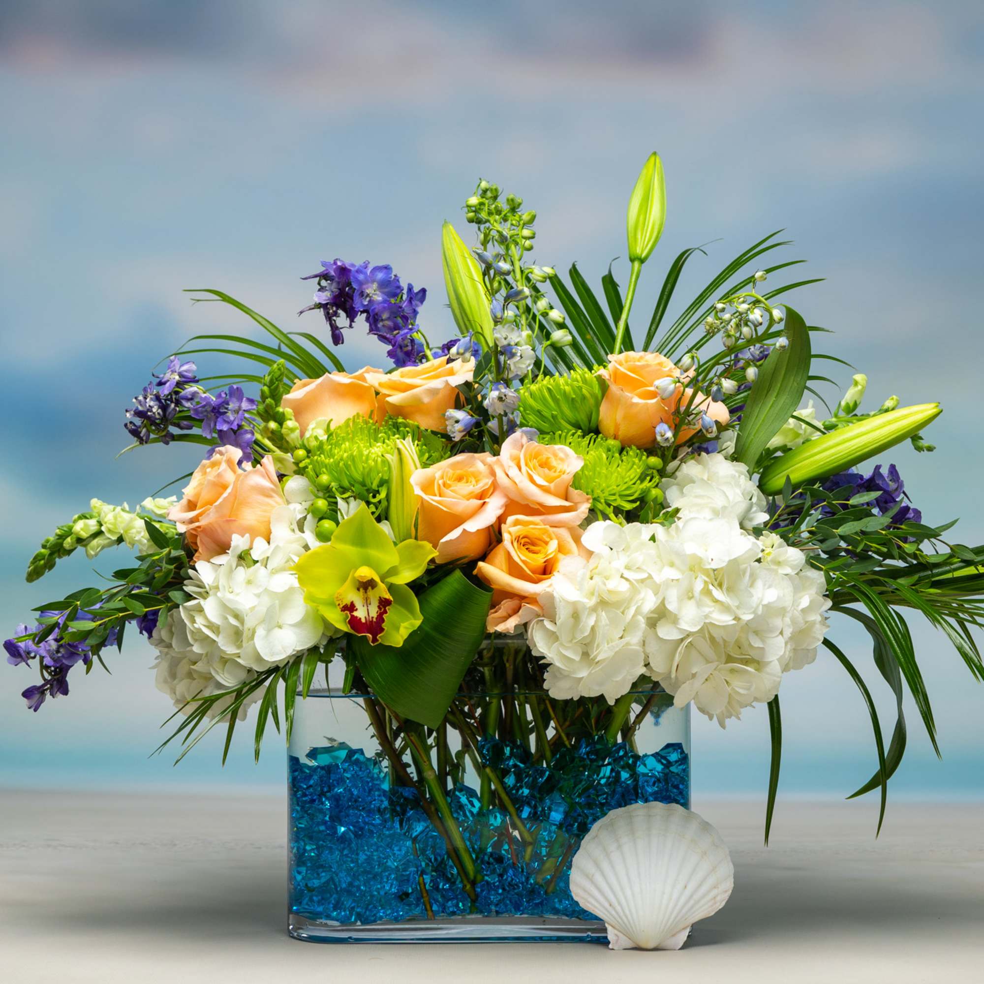 Arrangement of peach roses, white hydrangeas, and purple flowers in a blue vase