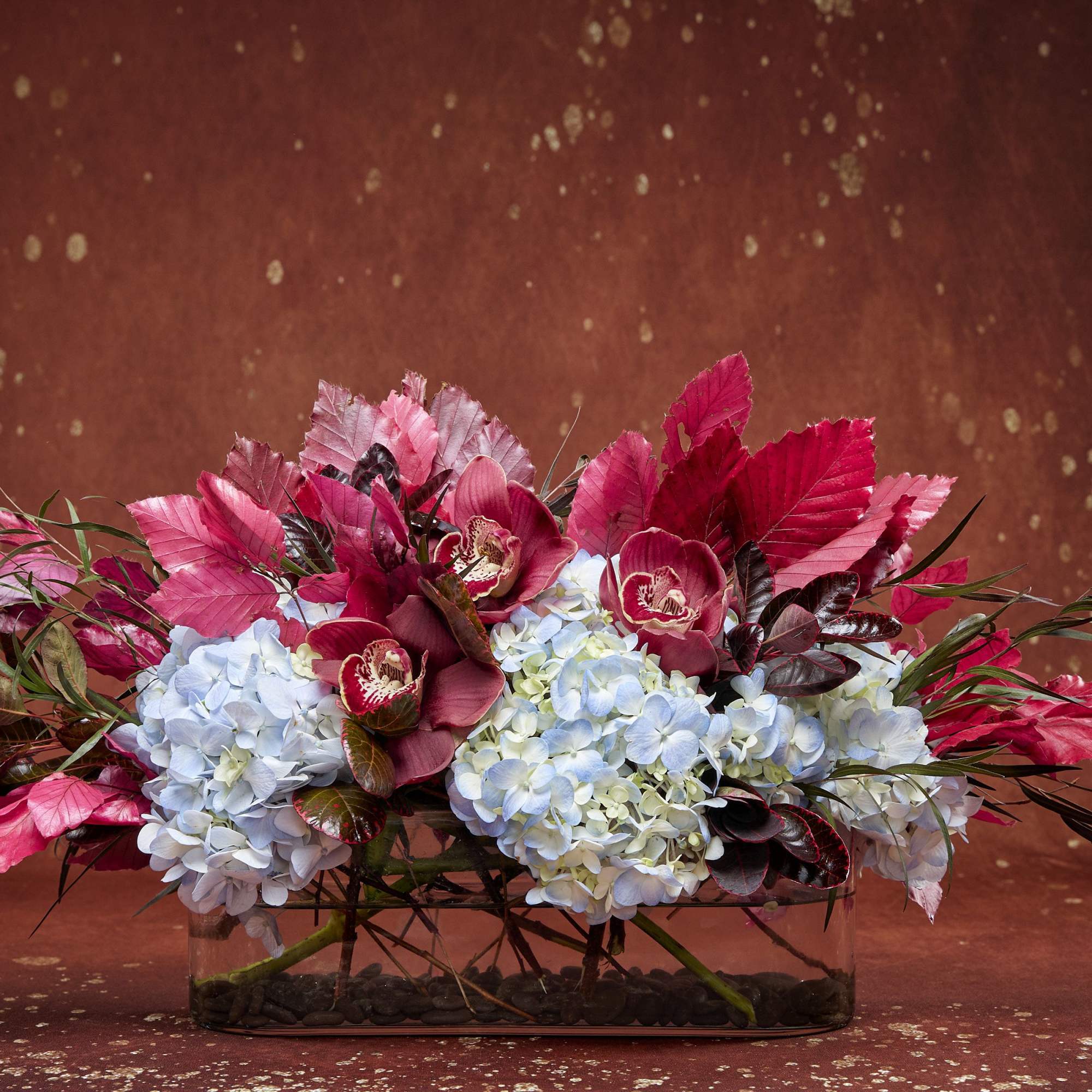 Low floral arrangement with blue hydrangeas and pink orchids in a glass container