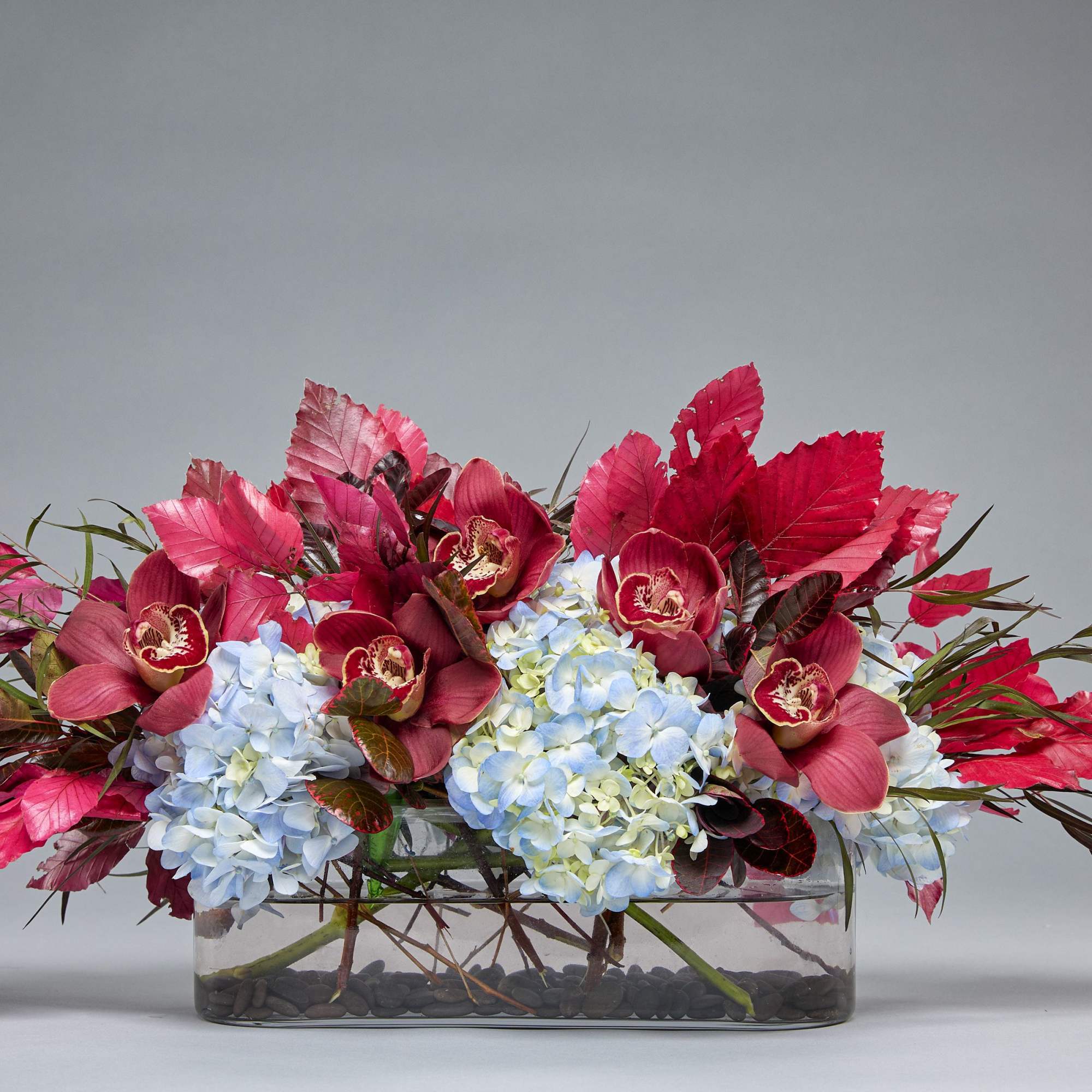 Low floral arrangement with blue hydrangeas and burgundy orchids in a glass vase