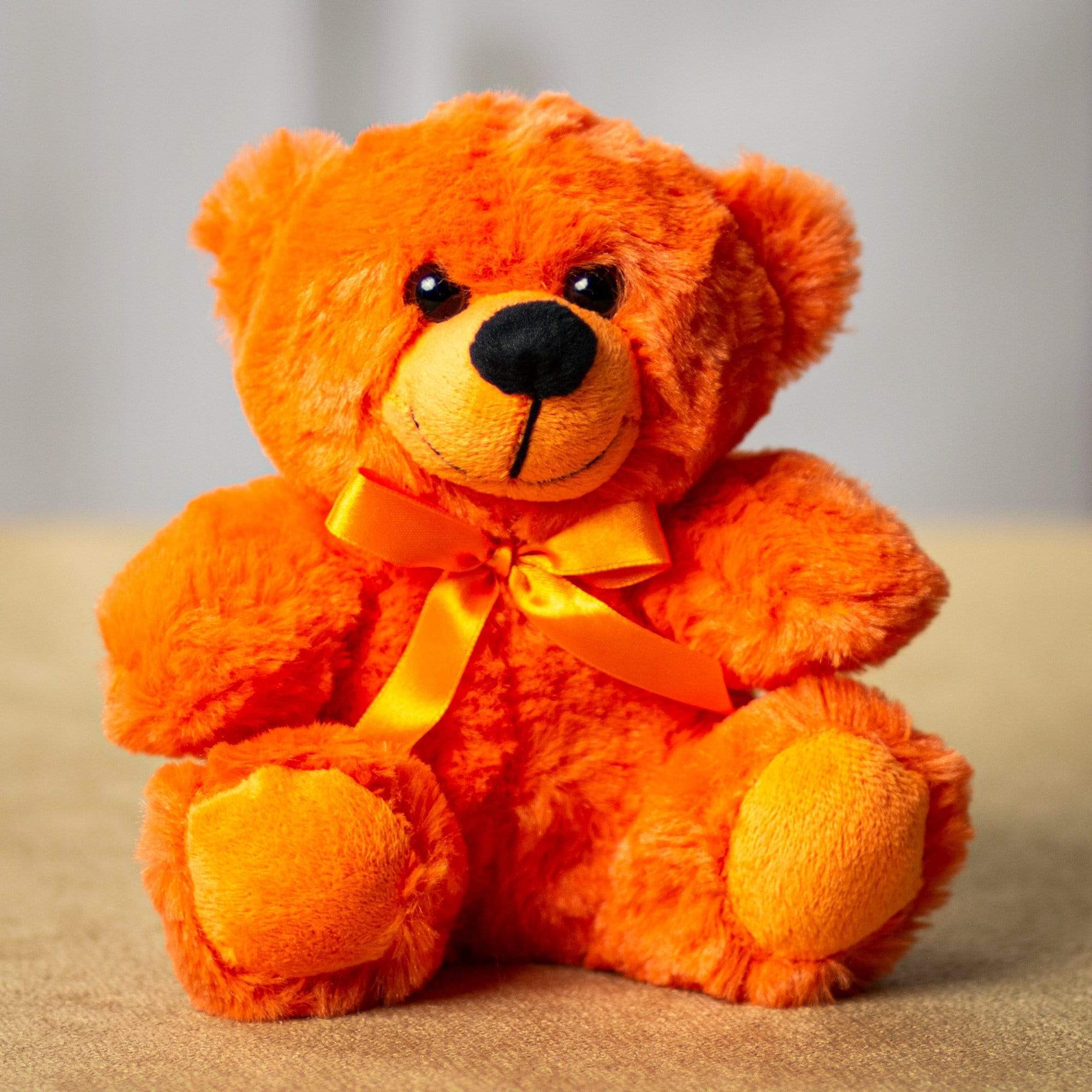 Orange teddy bear with a yellow ribbon sitting on a neutral surface