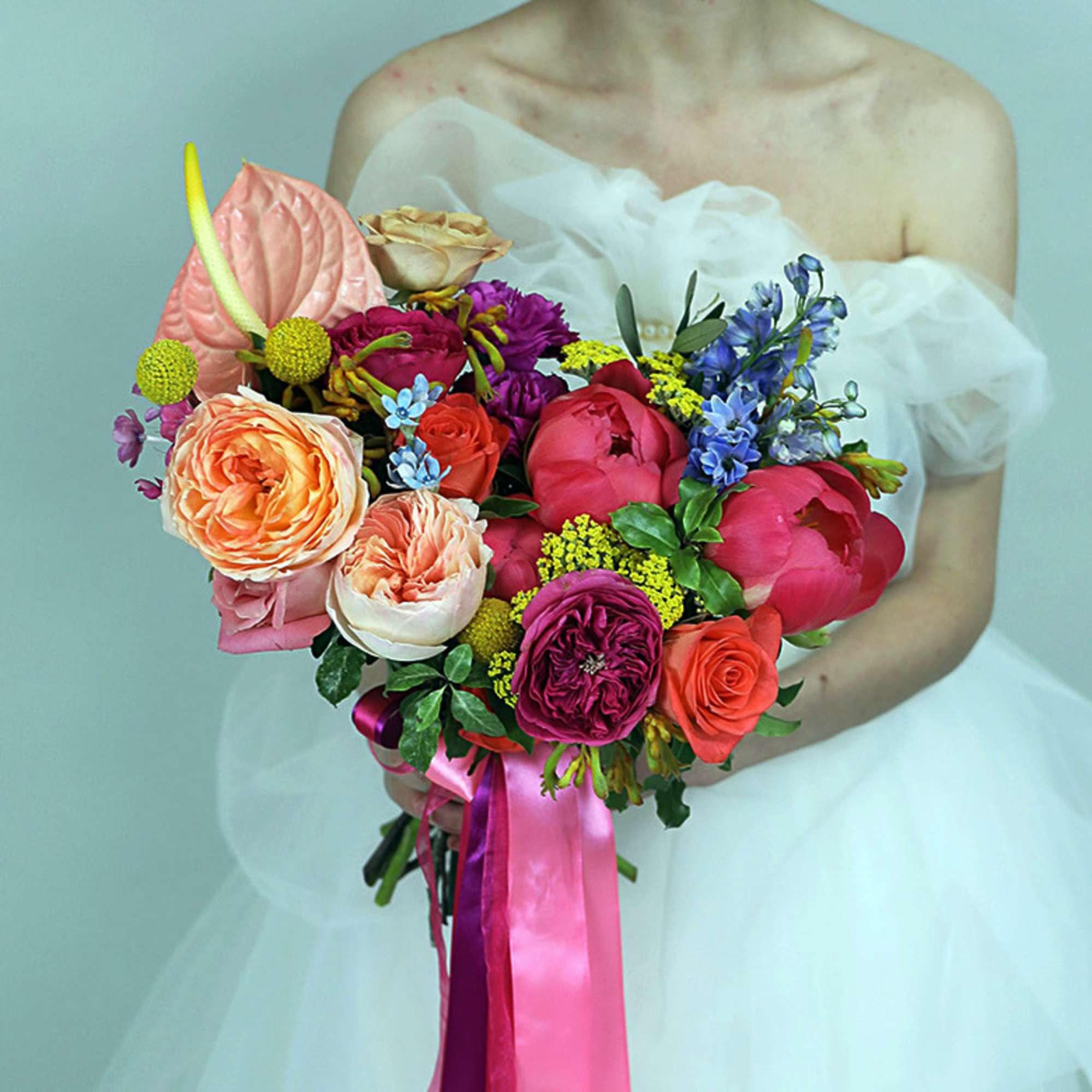 Bride holding a colorful bouquet of roses and mixed flowers with pink ribbon