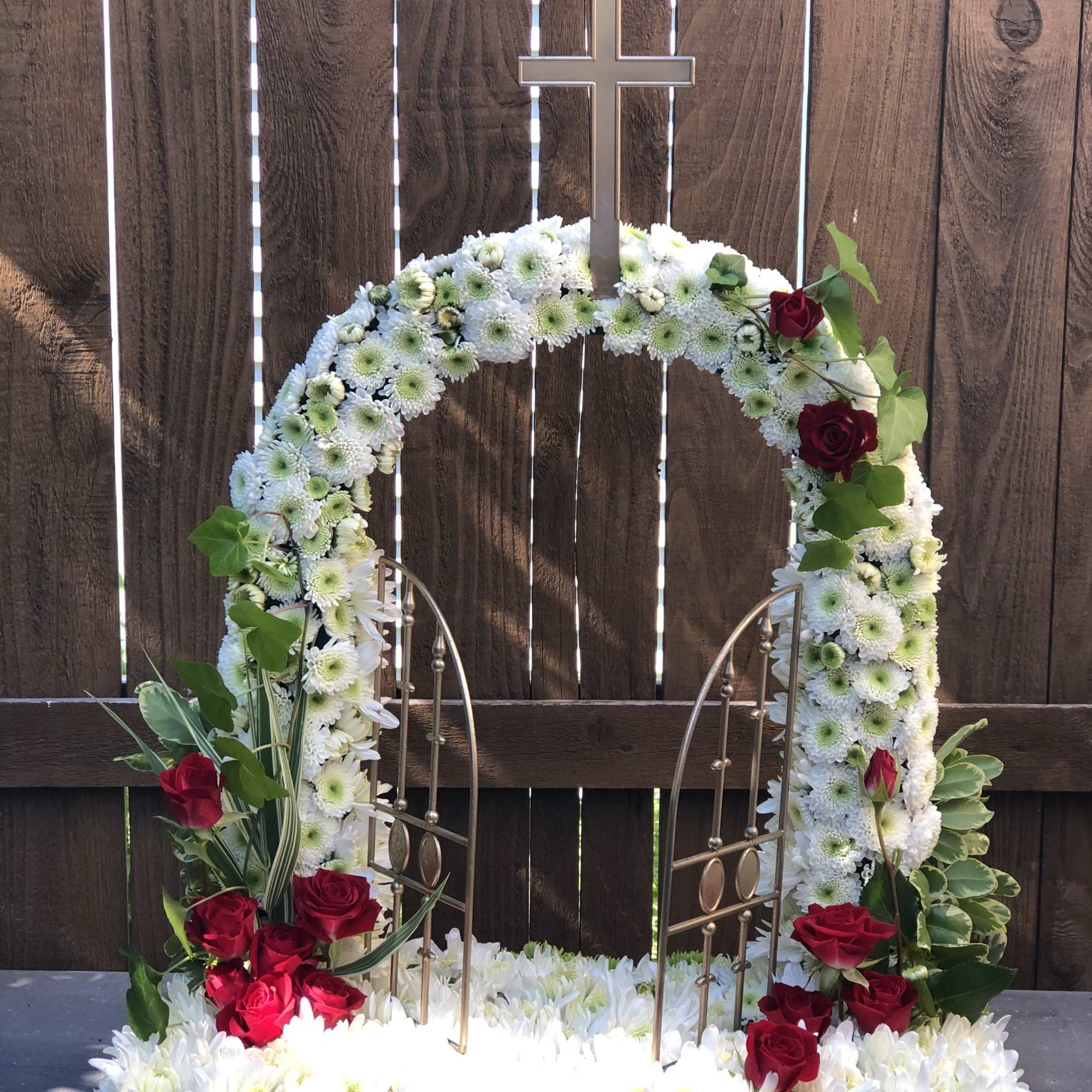 White floral funeral wreath with red roses and a cross topper