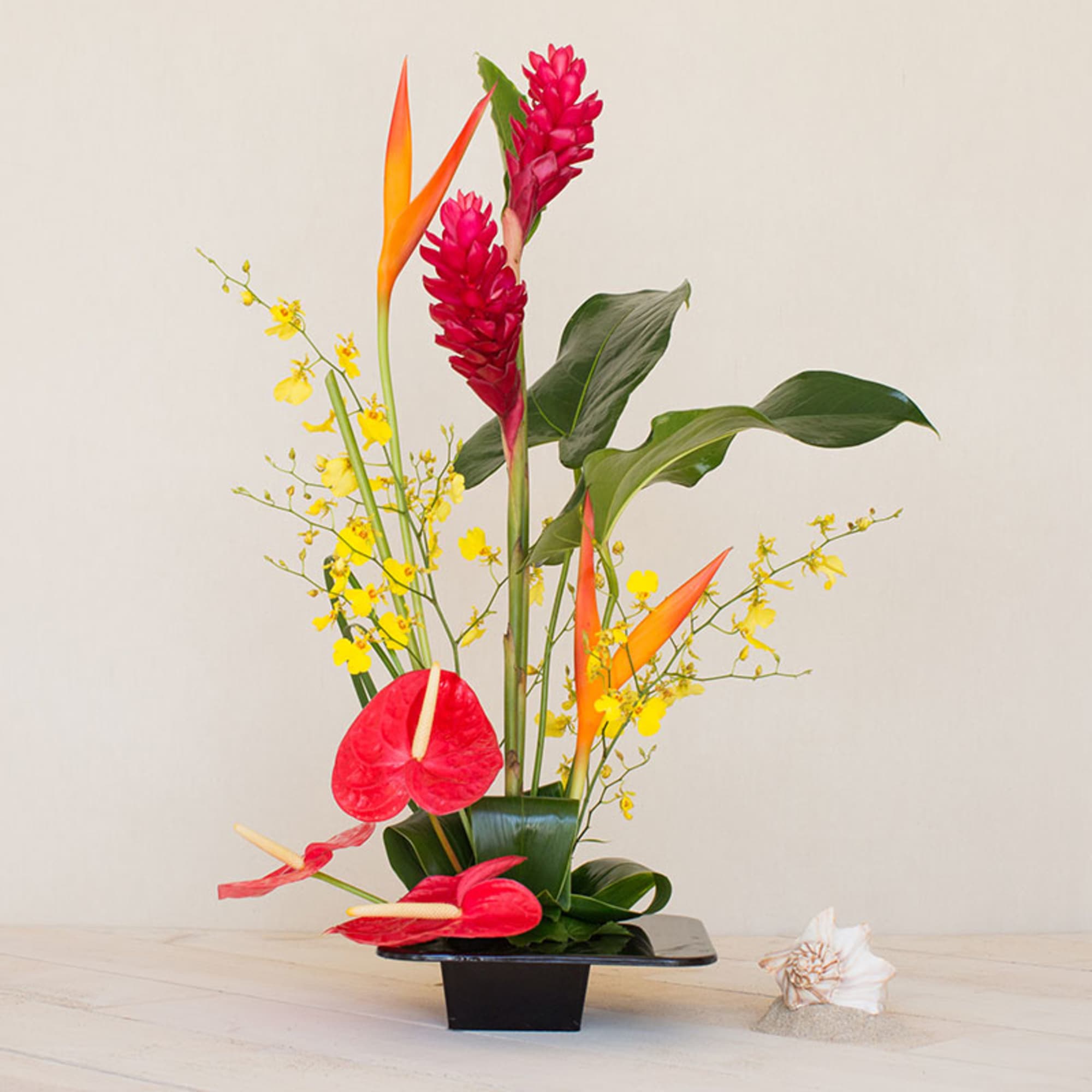 Tall tropical arrangement with red and yellow flowers in a black rectangular container.