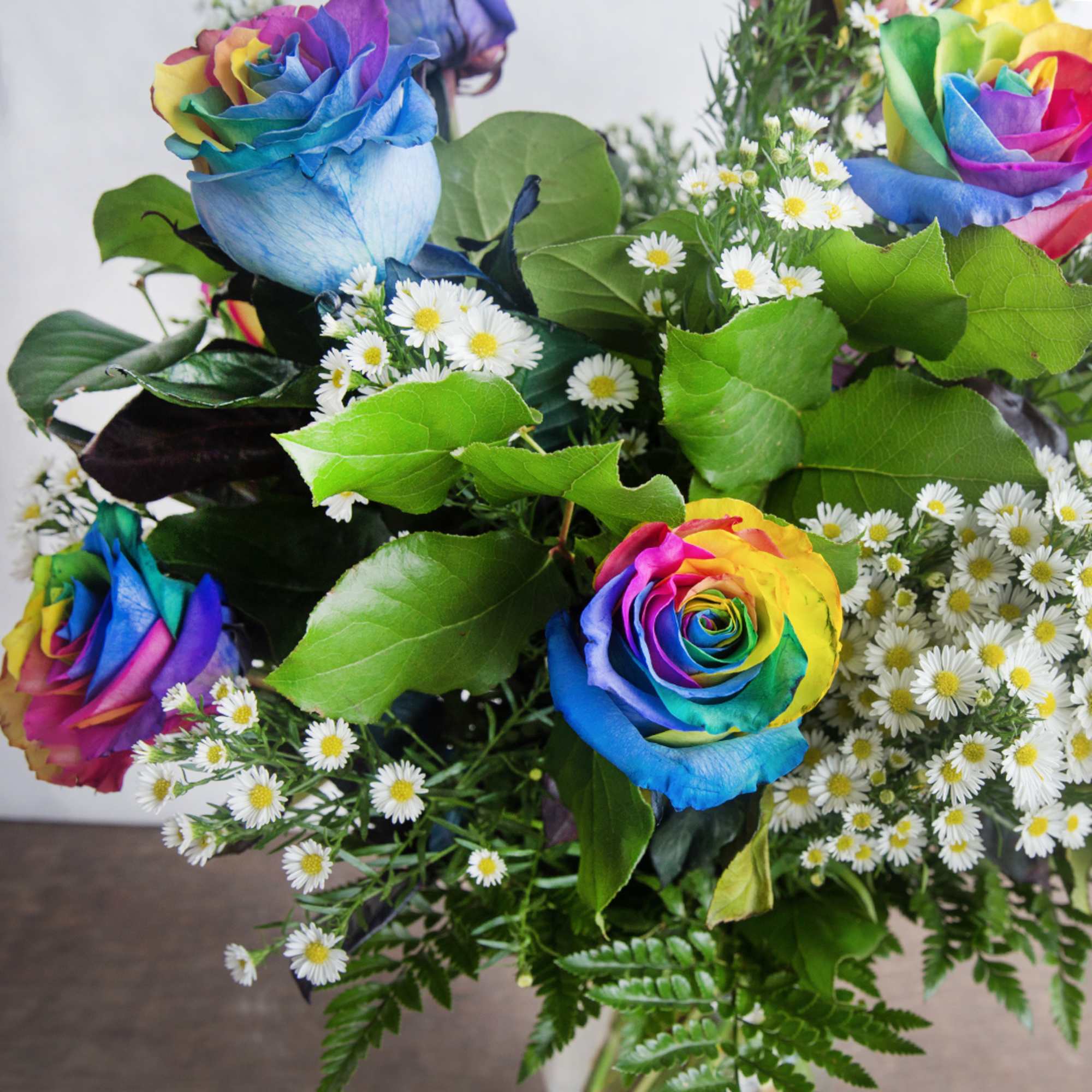 Arrangement of rainbow roses with small white daisy flowers