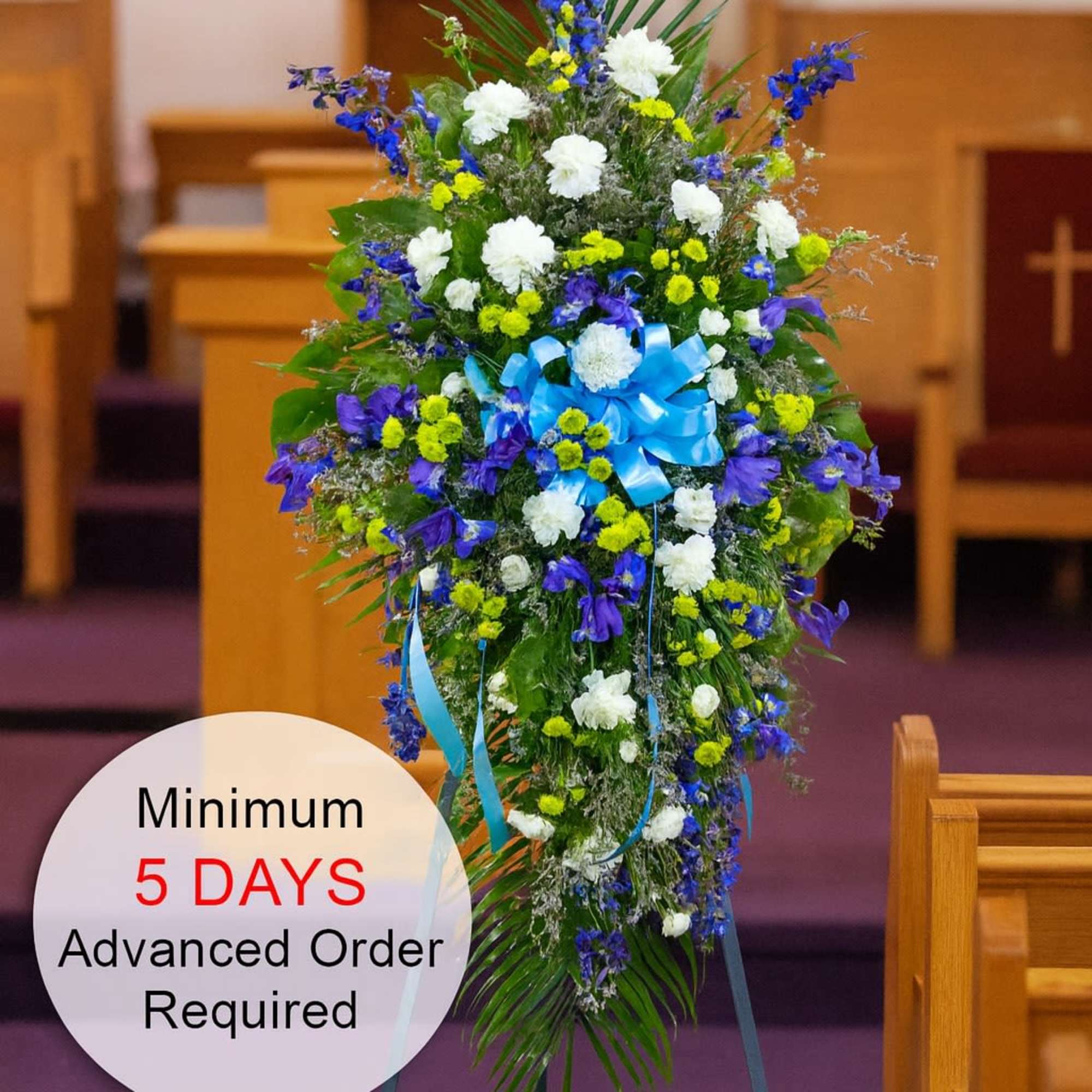 Tall blue, white, and yellow standing spray with bow on an easel in a church setting