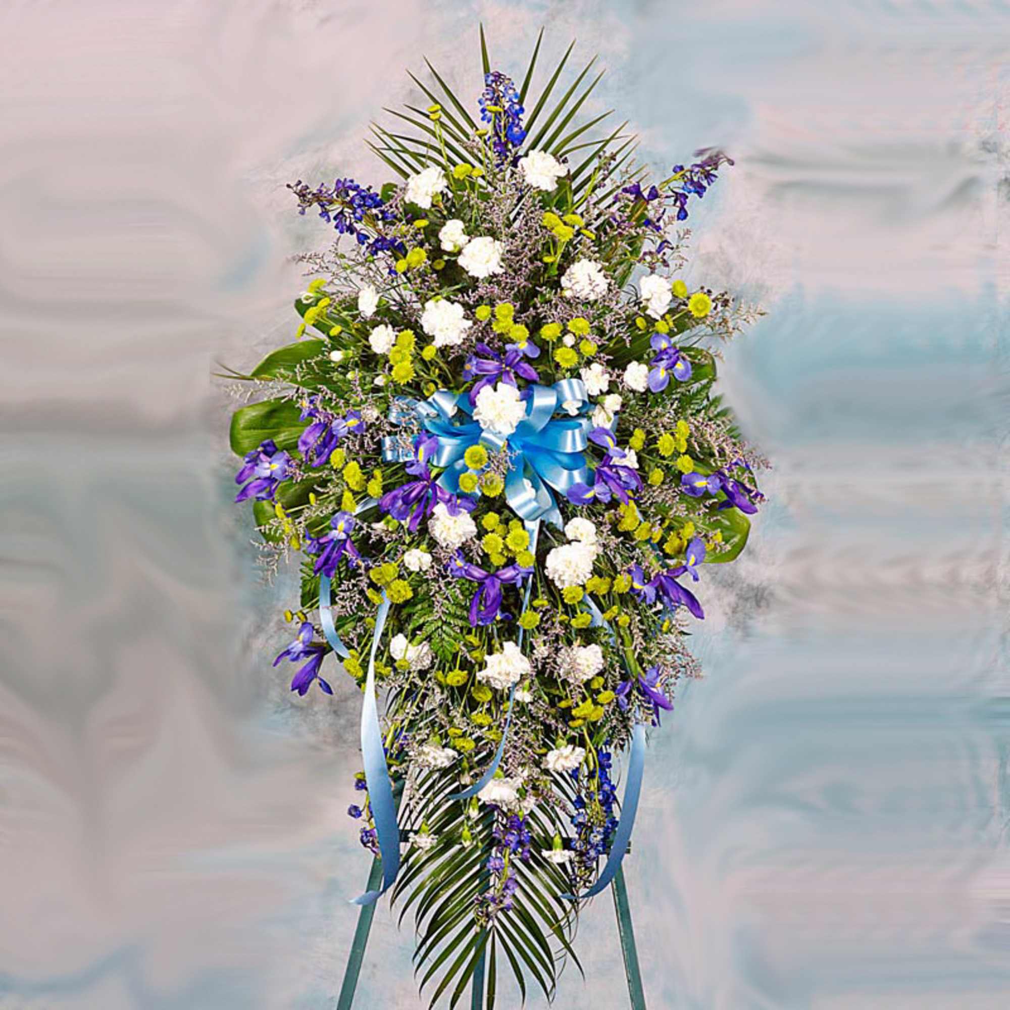 Tall standing spray of blue, white, and green flowers with a blue bow on an easel.
