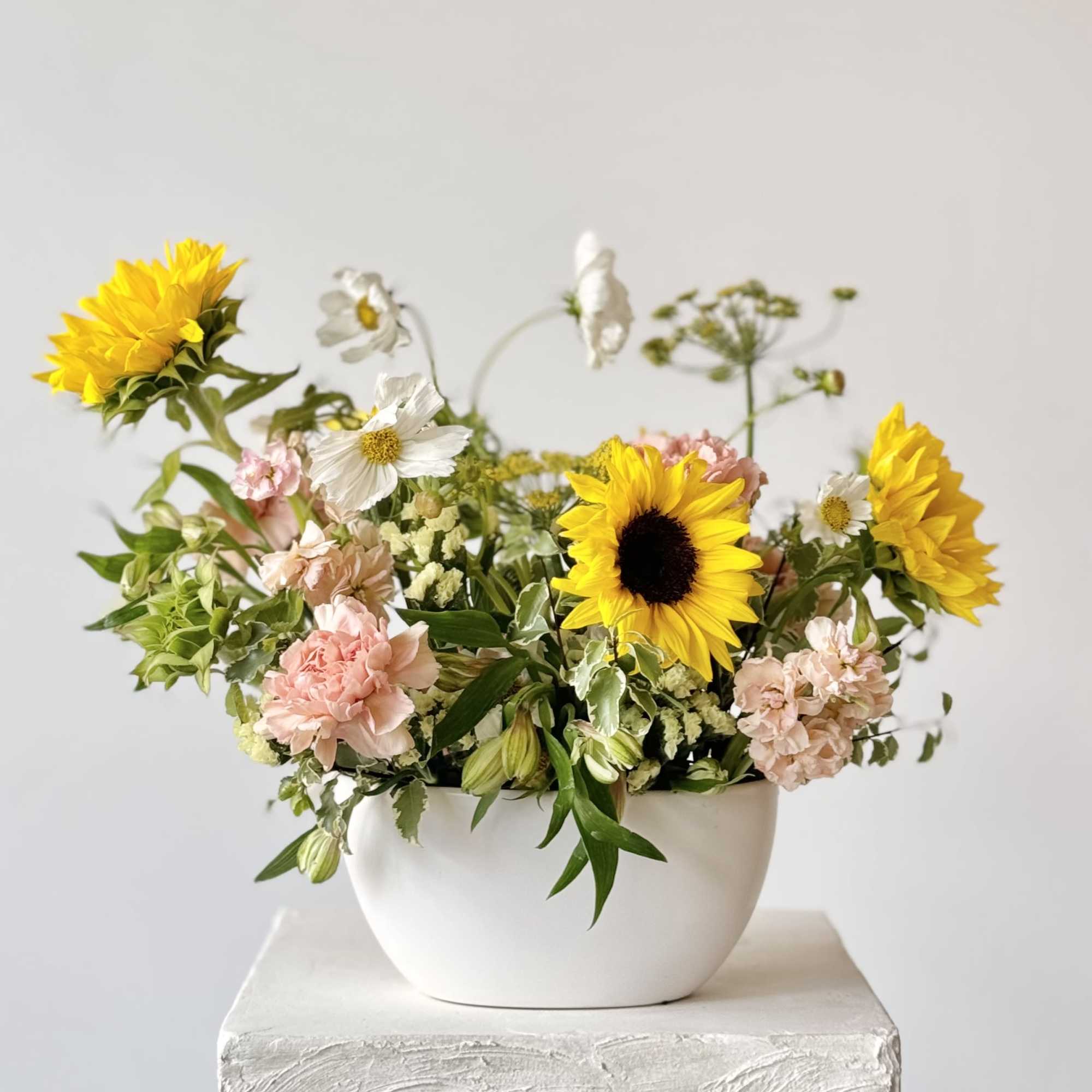 Mixed bouquet with sunflowers, pink carnations, and white daisies in a white bowl