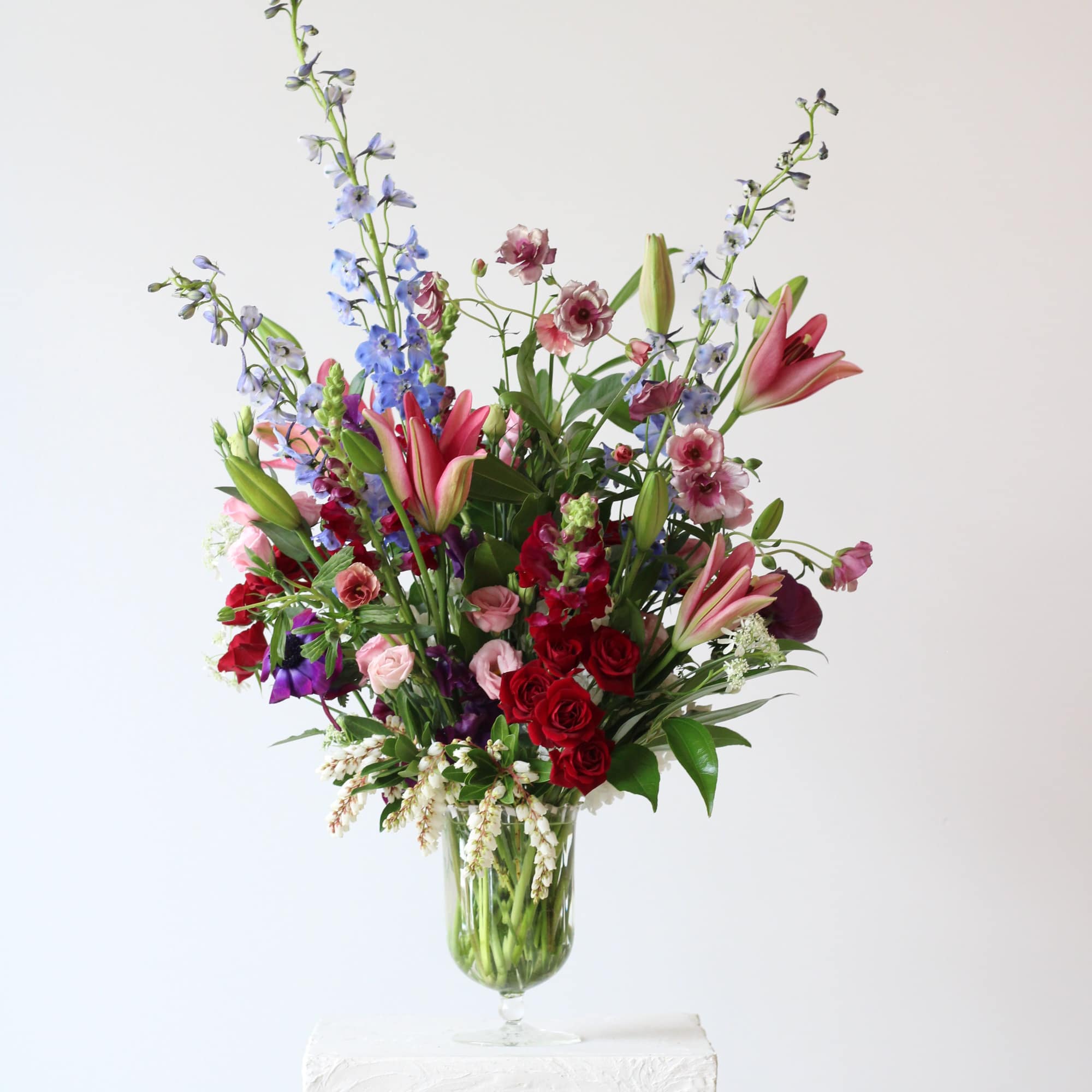 Tall mixed bouquet in a glass vase with lilies, roses, and blue spikes