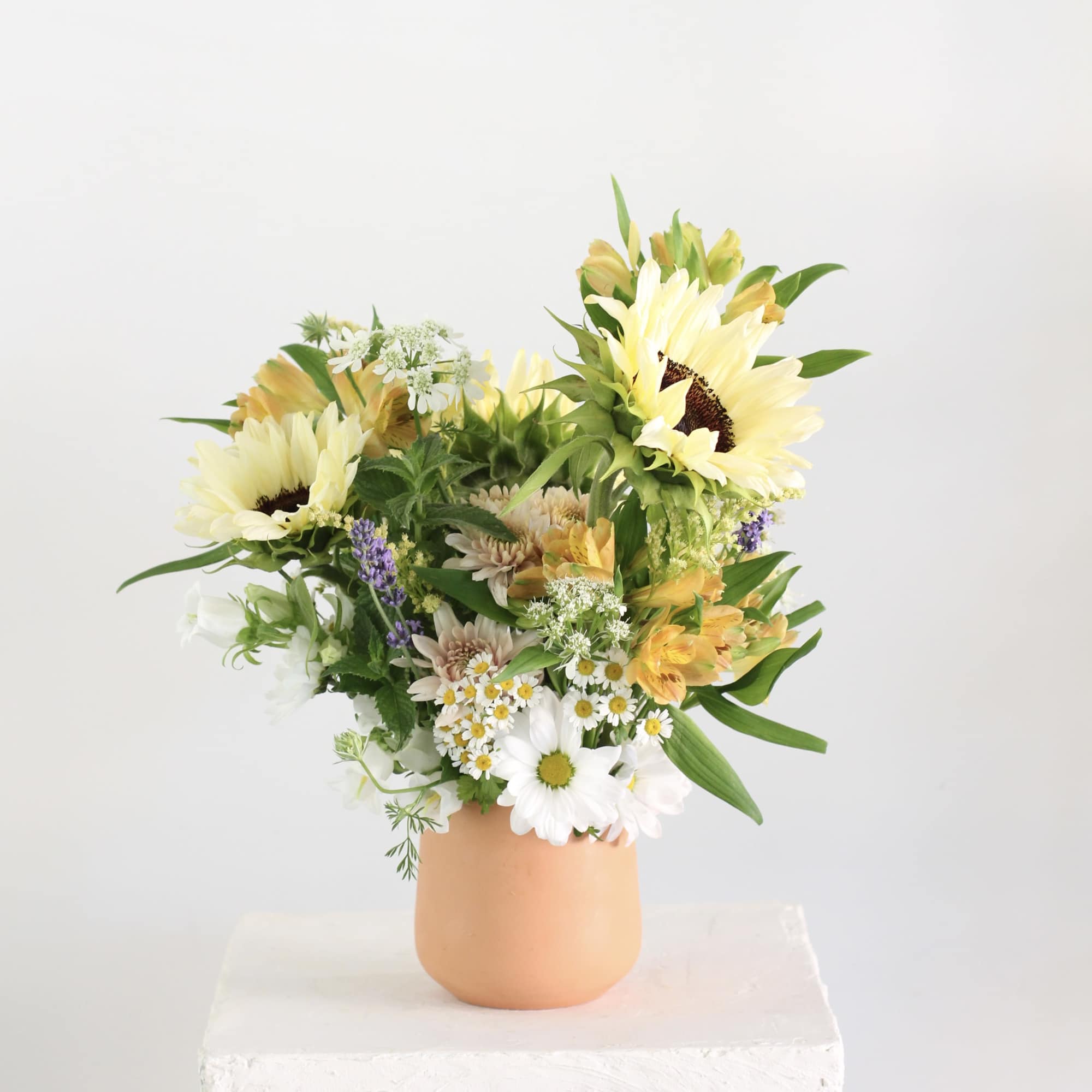 Mixed bouquet with sunflowers and daisies in a peach vase