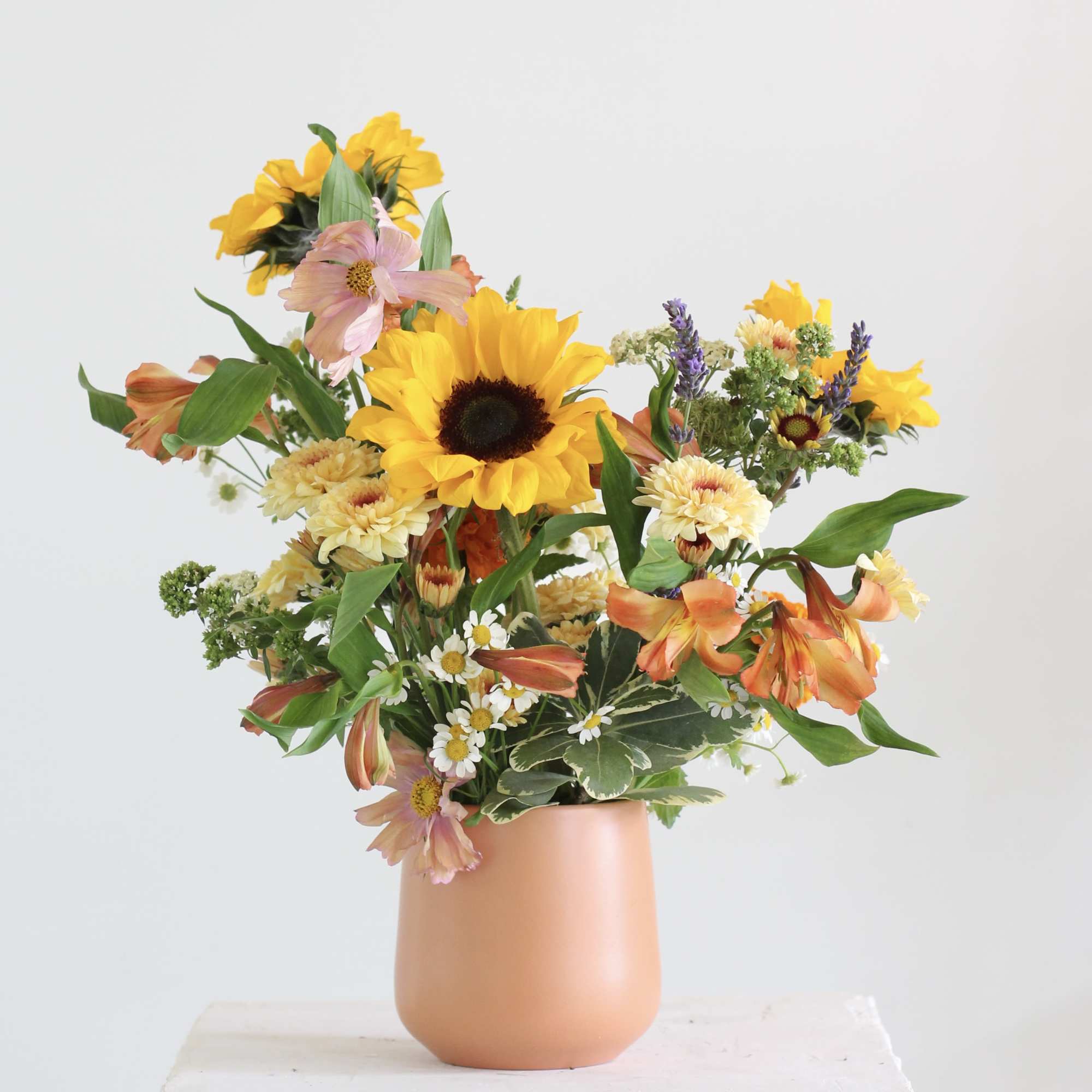 Mixed bouquet with sunflowers and orange blooms in a peach vase