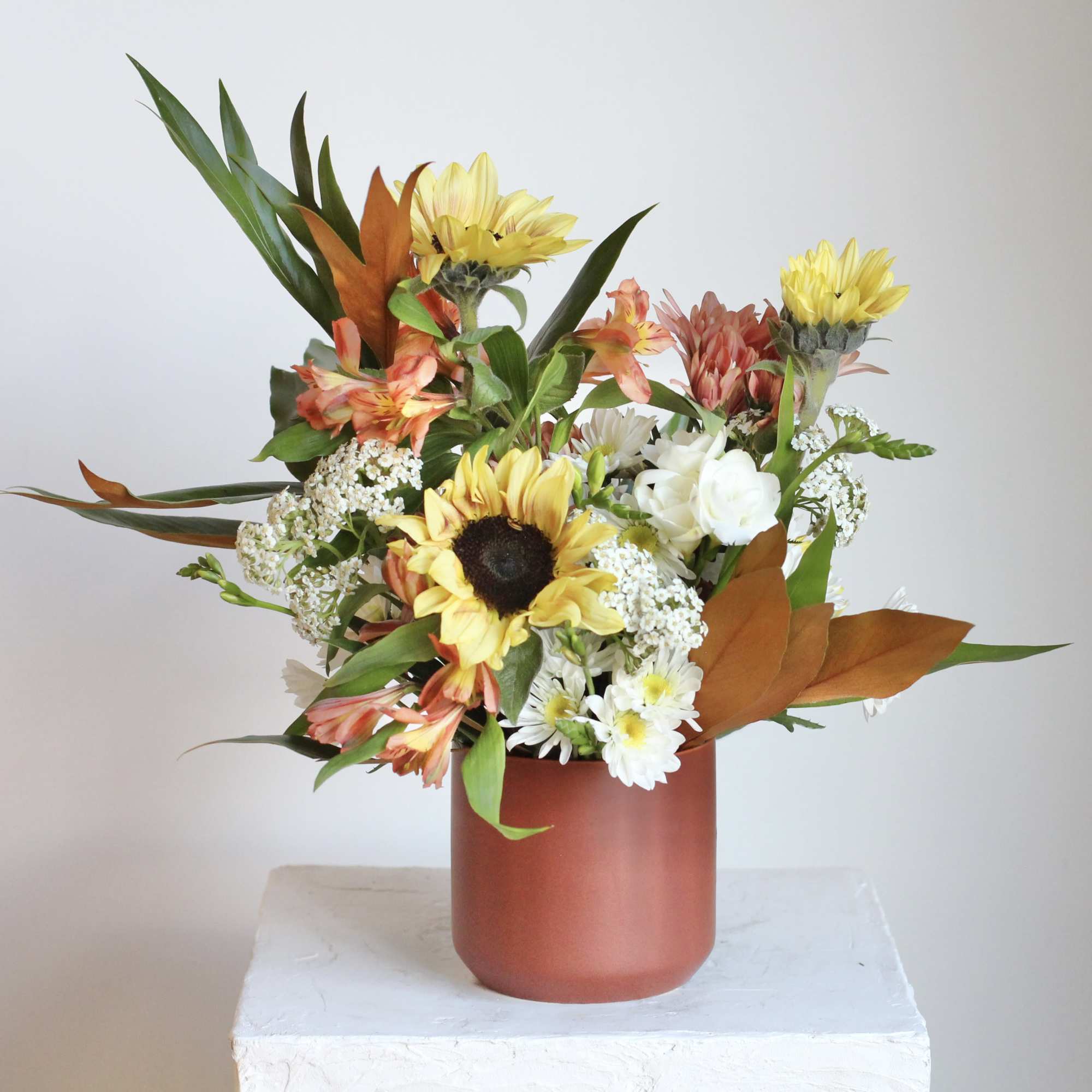 Mixed bouquet with sunflowers and white daisies in a rust-colored vase