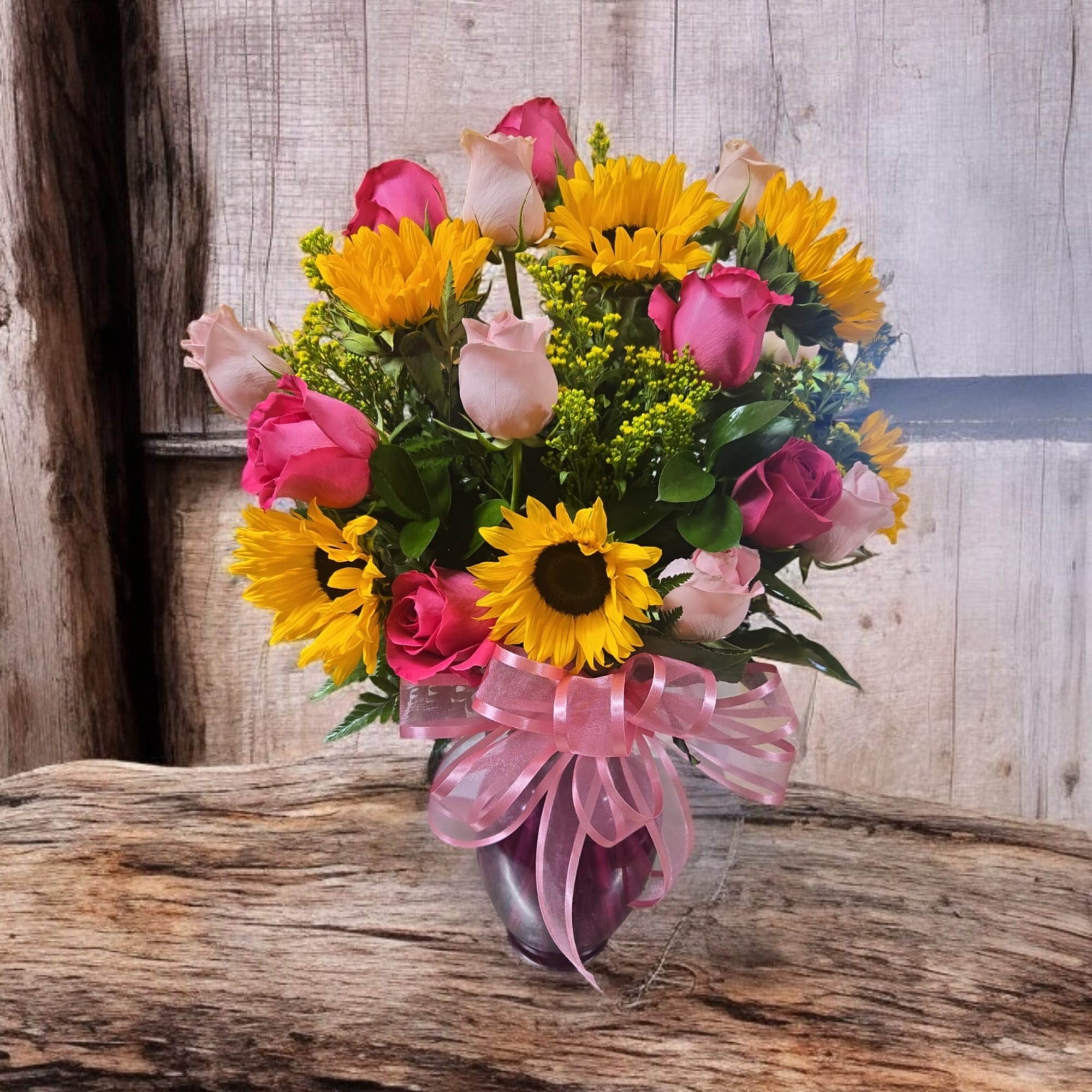 Bouquet of pink roses and yellow sunflowers in a glass vase with a pink ribbon
