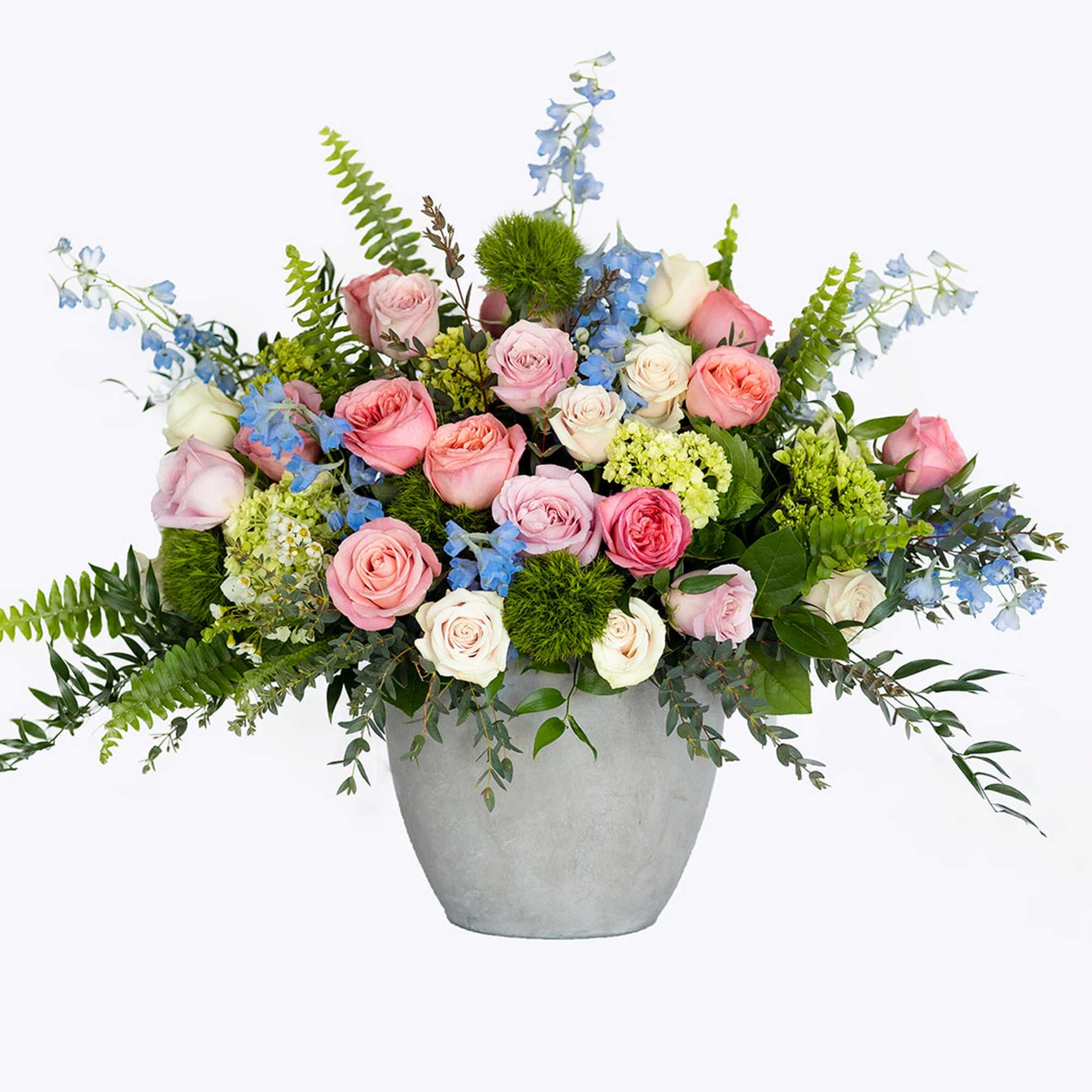 Wide arrangement of pink and cream roses with blue flowers and ferns in a gray pot