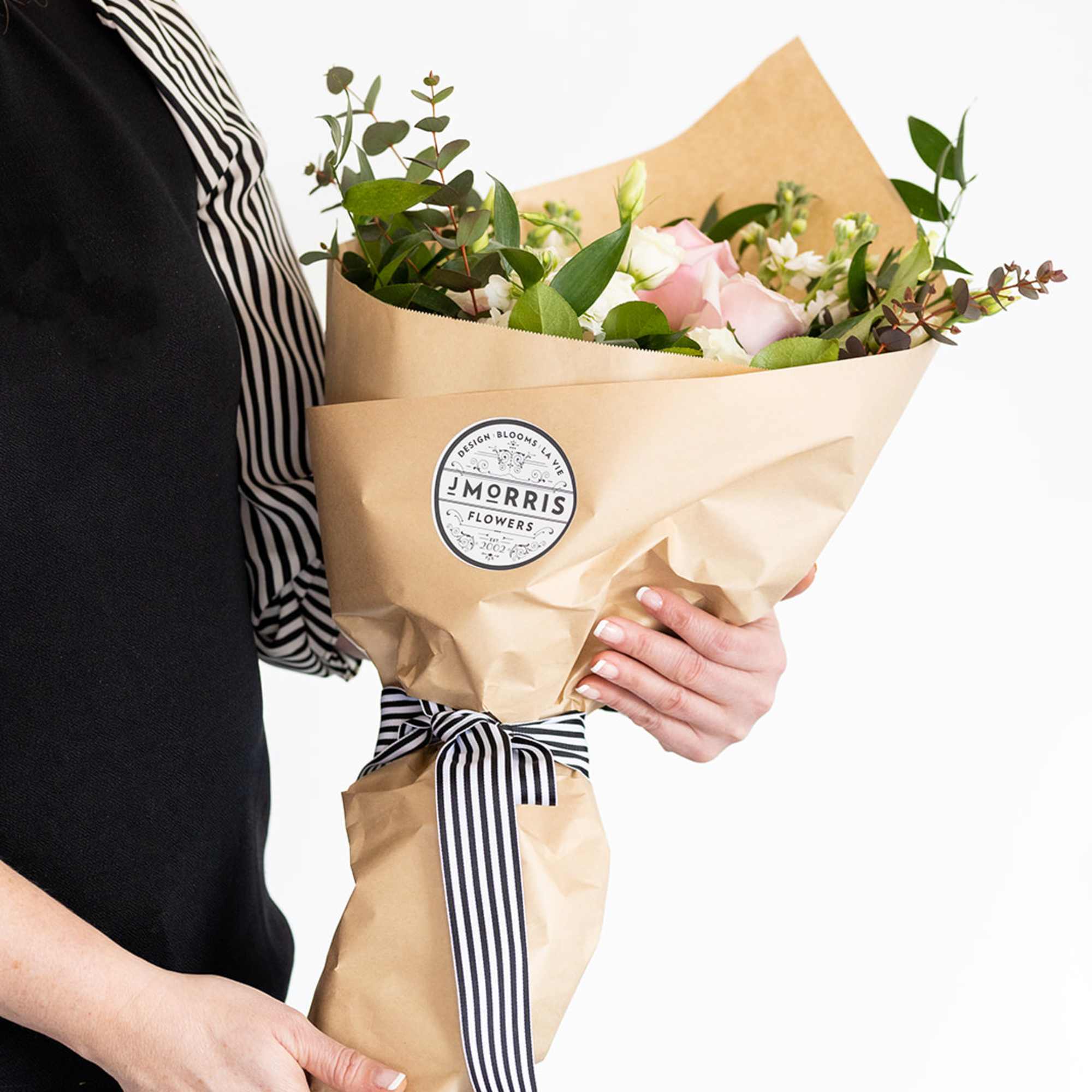 Handheld bouquet of pink and white roses wrapped in kraft paper