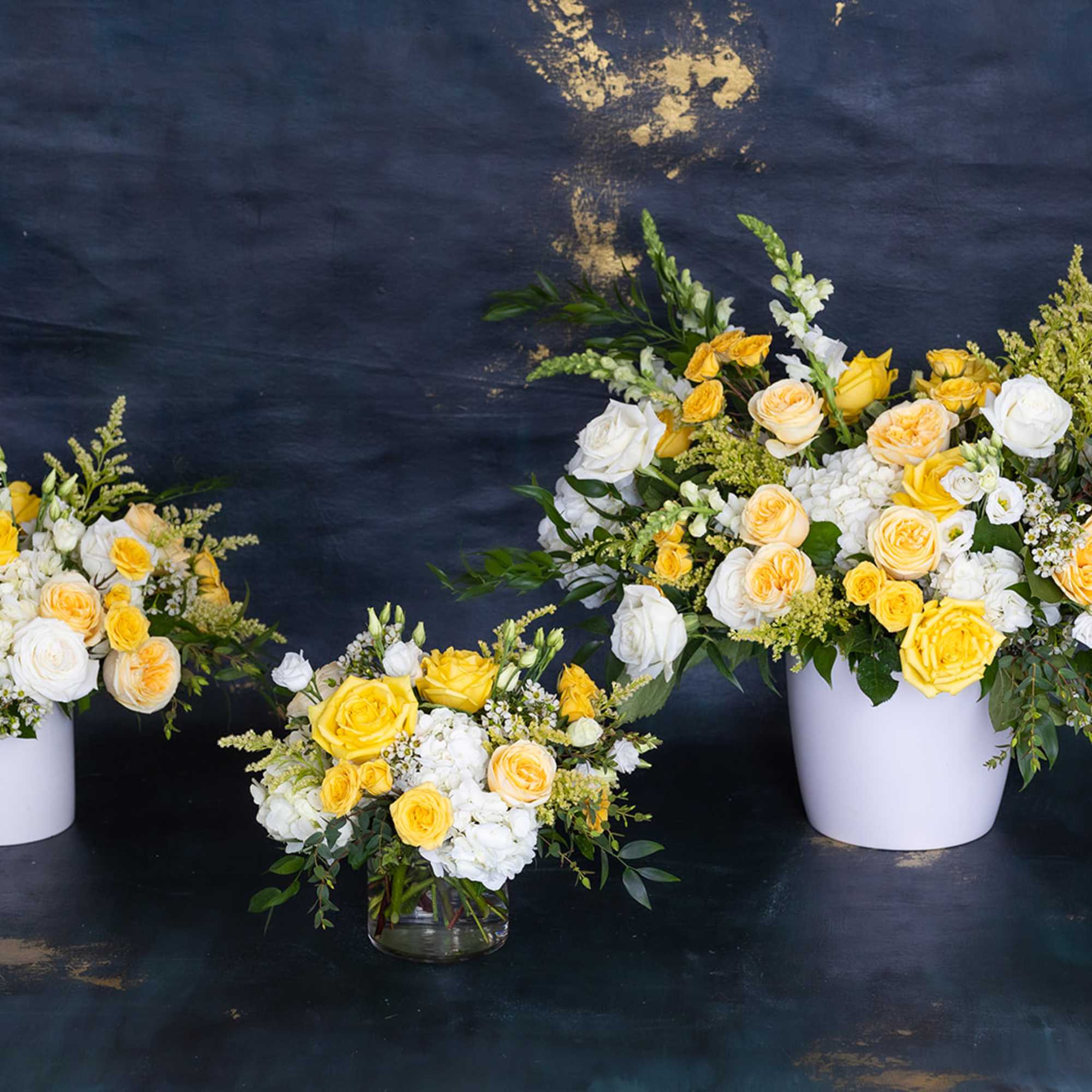 Yellow and white rose arrangements in white containers and a glass vase