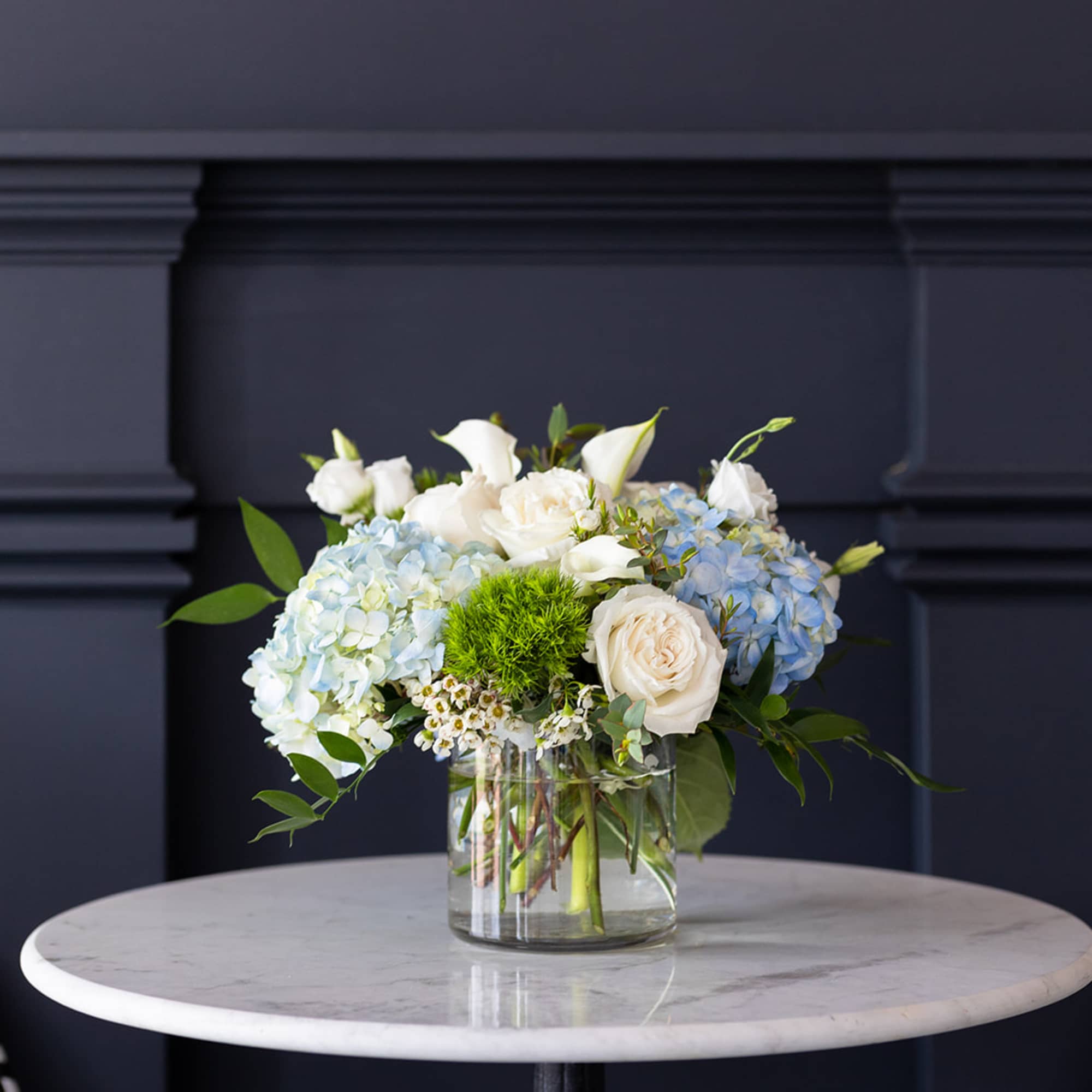 White and blue floral arrangement in a clear glass vase