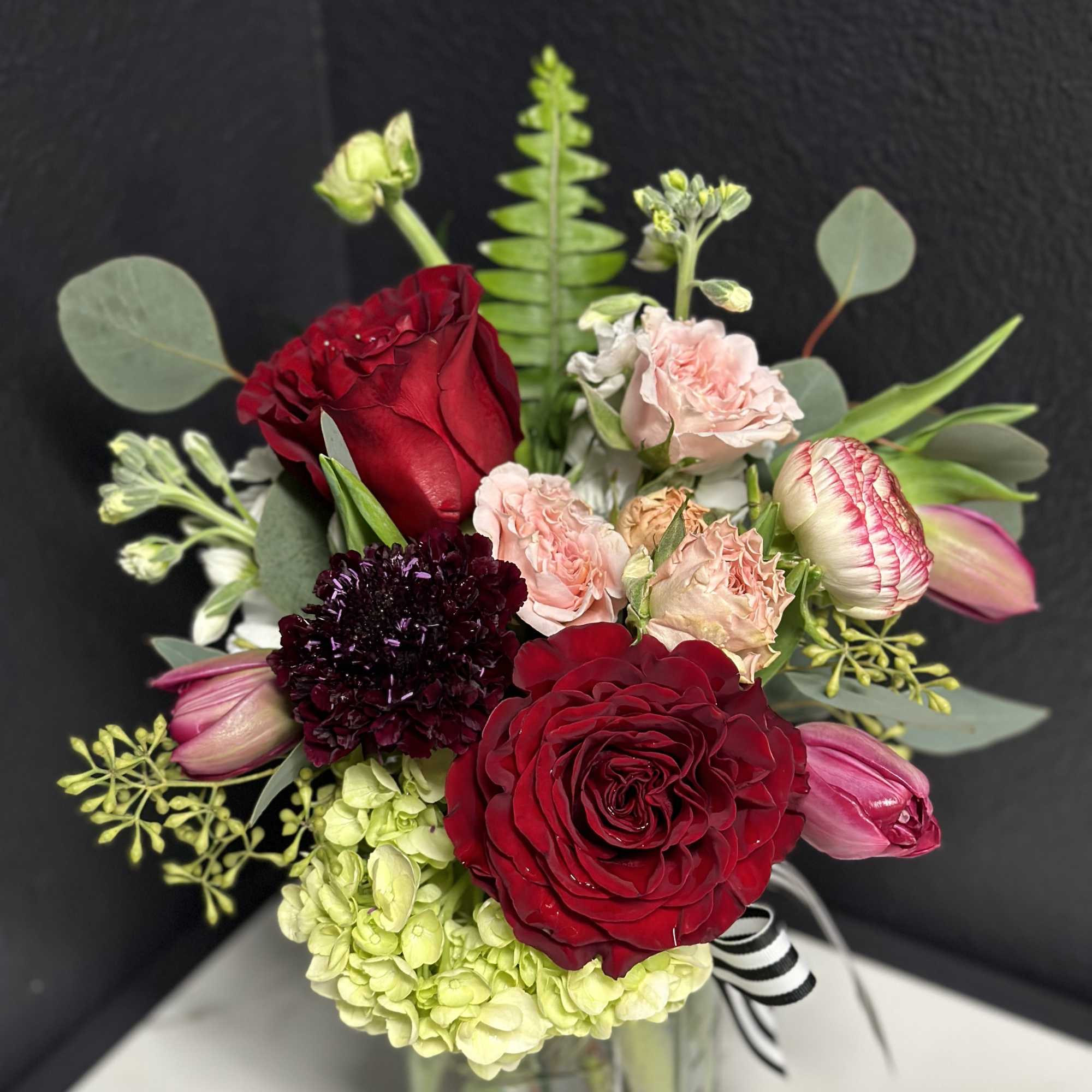 Bouquet of red roses, pink blooms, and pale green hydrangea in a vase
