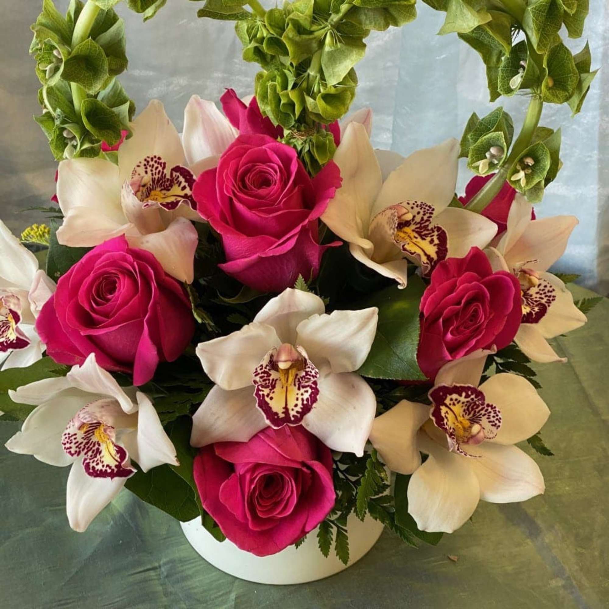 Pink roses and white orchids in a white container with a green floral arch