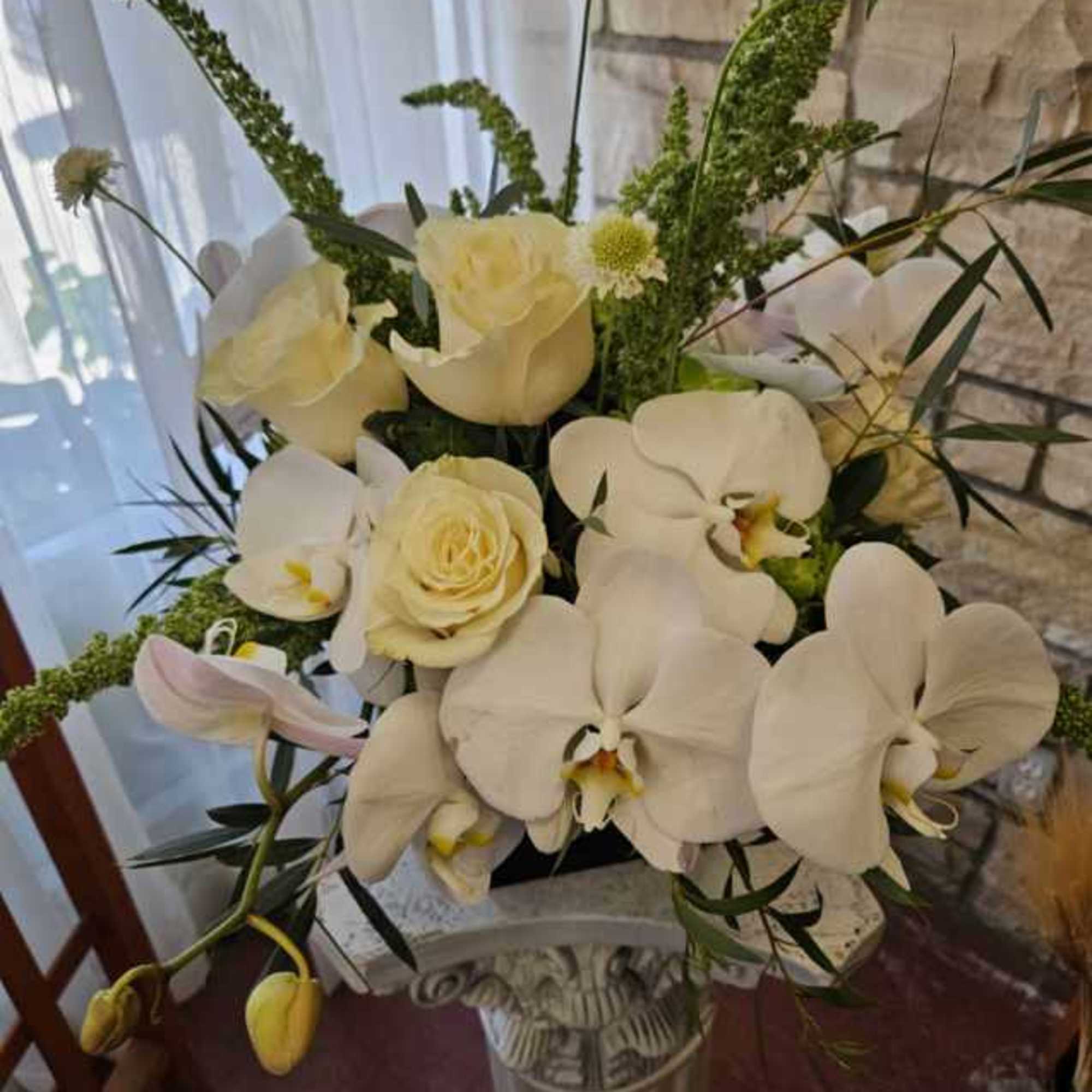 White orchids and cream roses in a tall silver vase