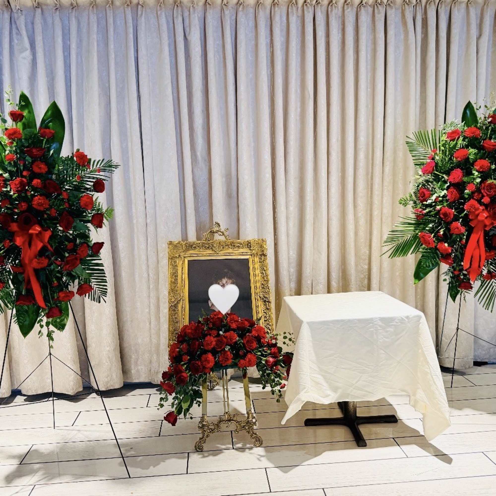 Red rose funeral display with standing sprays and a framed heart tribute